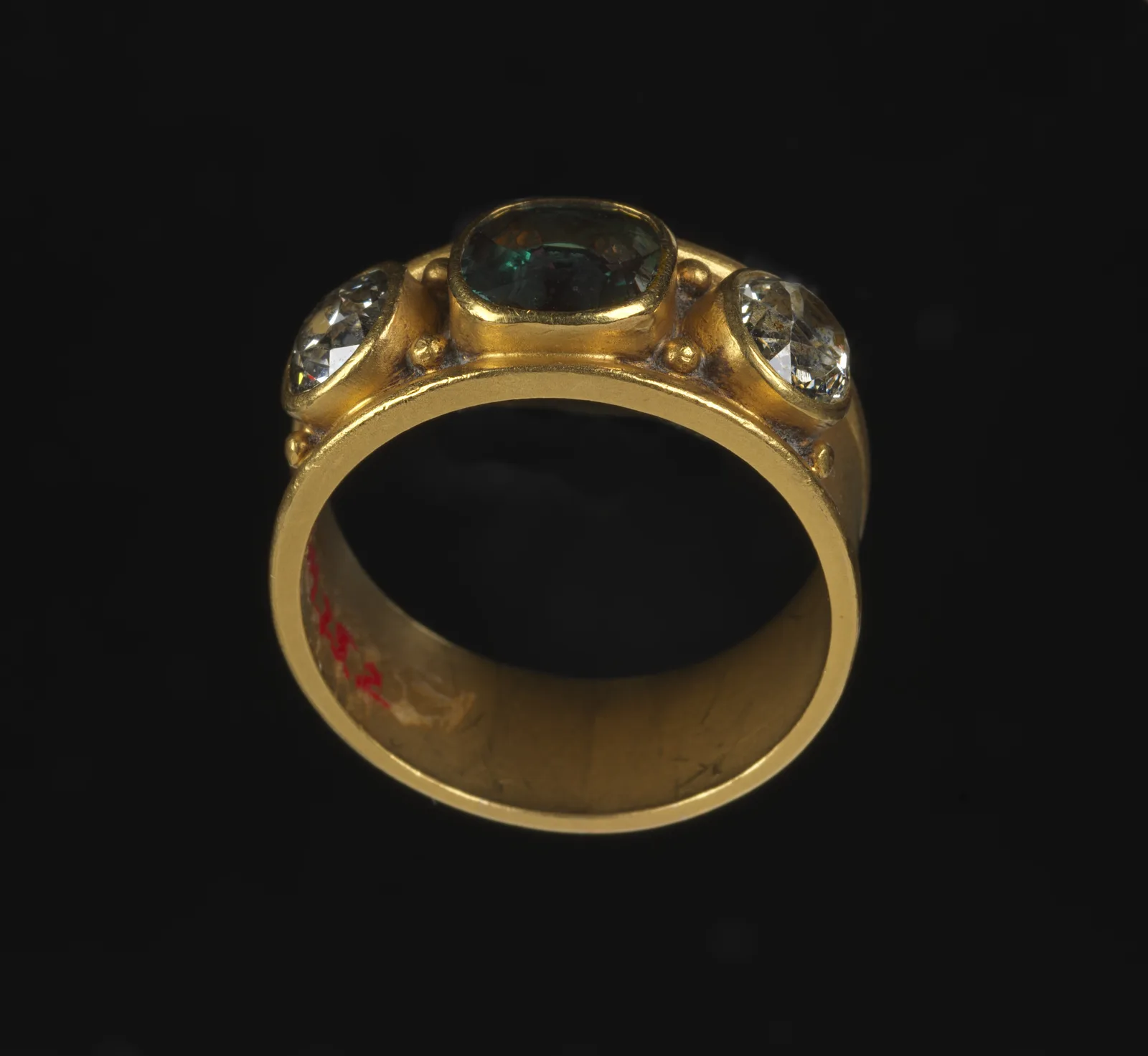 Gold ring with a diamond and a small green alexandrite inset, a museum catalog still on a gray ground