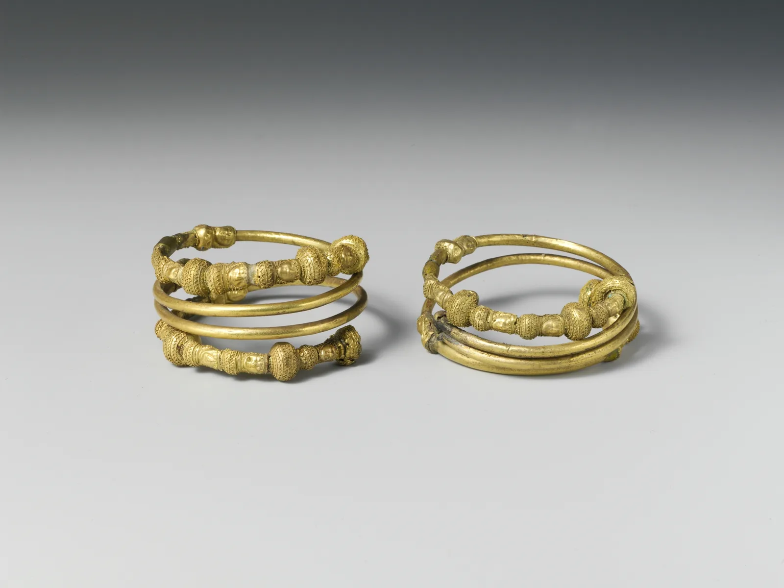 Pair of Etruscan electrum bracelet spirals, each a tight spring of gold-colored coils with beaded and granulated turns