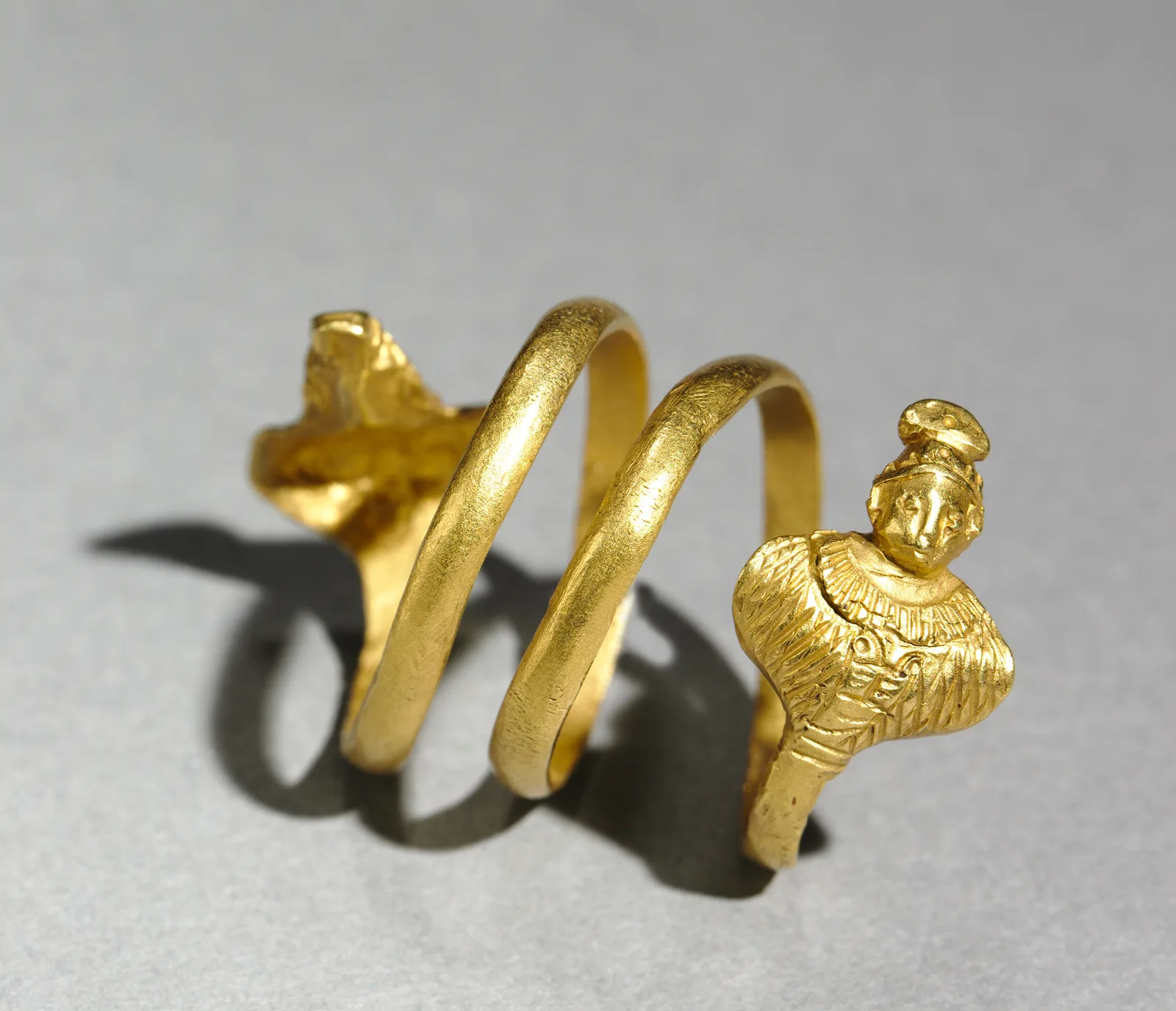 Roman gold spiral ring of two and a half turns ending in a small bust of Isis or Serapis and a flared opposing terminal