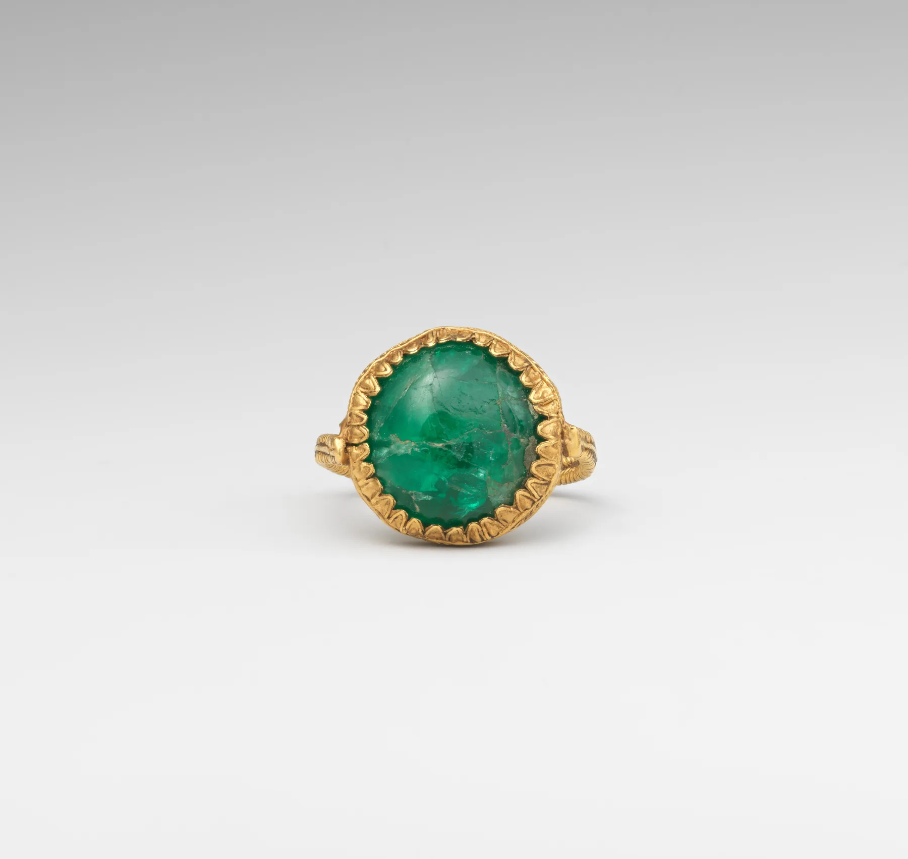 Greek gold ring with a round emerald cabochon held in a scalloped bezel on a textured gold hoop