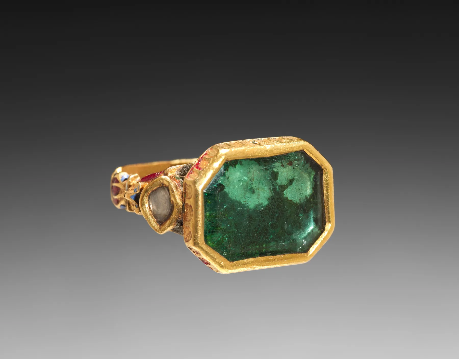 Mughal gold ring with a large green emerald in a thick rub-over bezel, enameled shoulders with side stones
