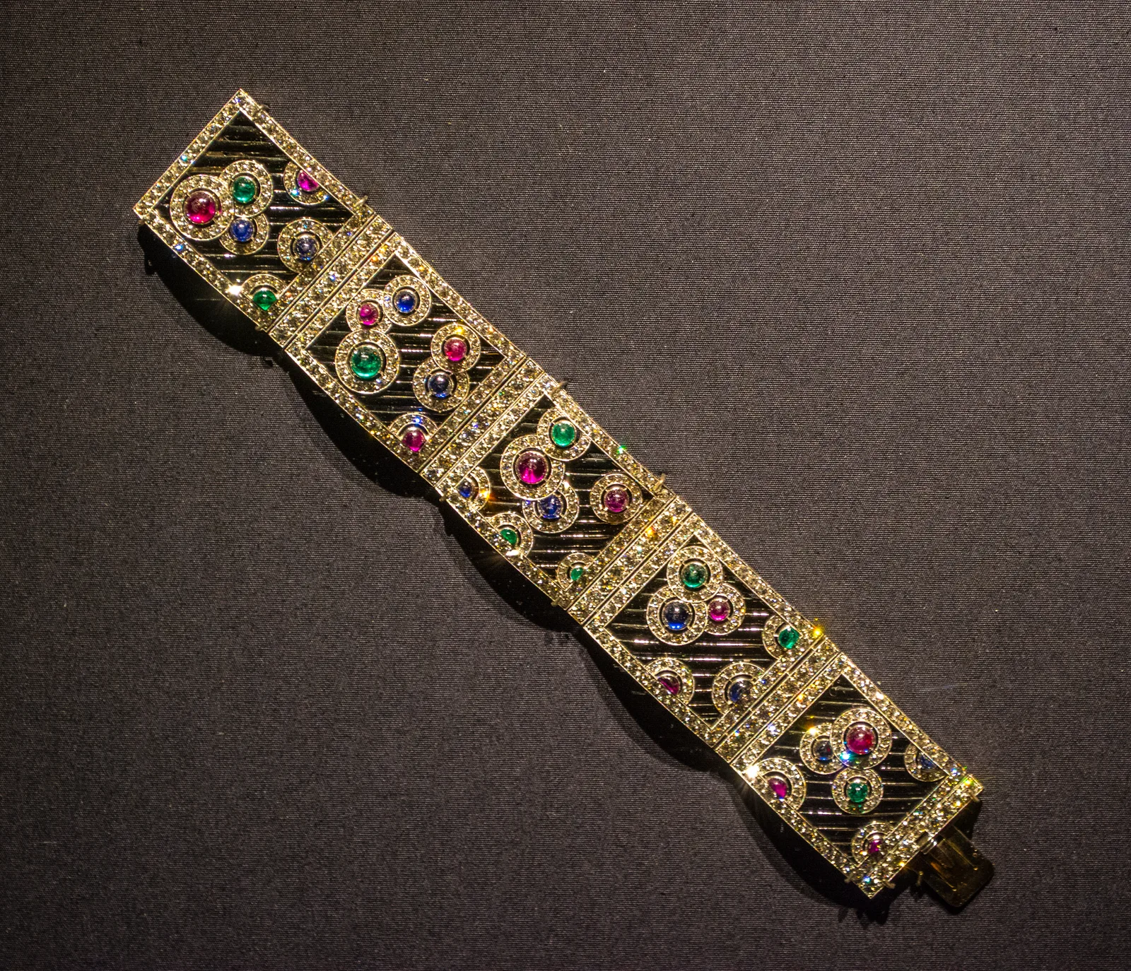 Boucheron articulated bracelet of square gold and diamond panels with colored cabochons on a dark ground