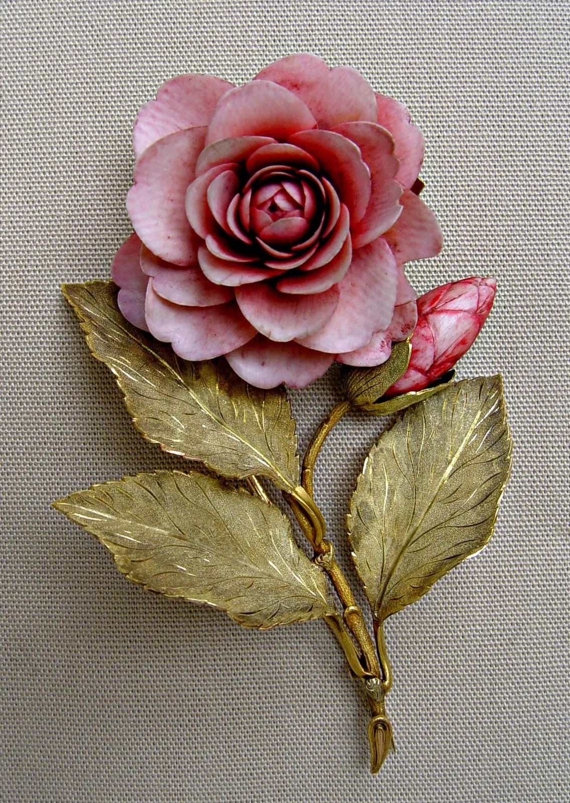 Victorian gold brooch formed as a camellia with tinted ivory petals, a closed bud, and engraved gold leaves