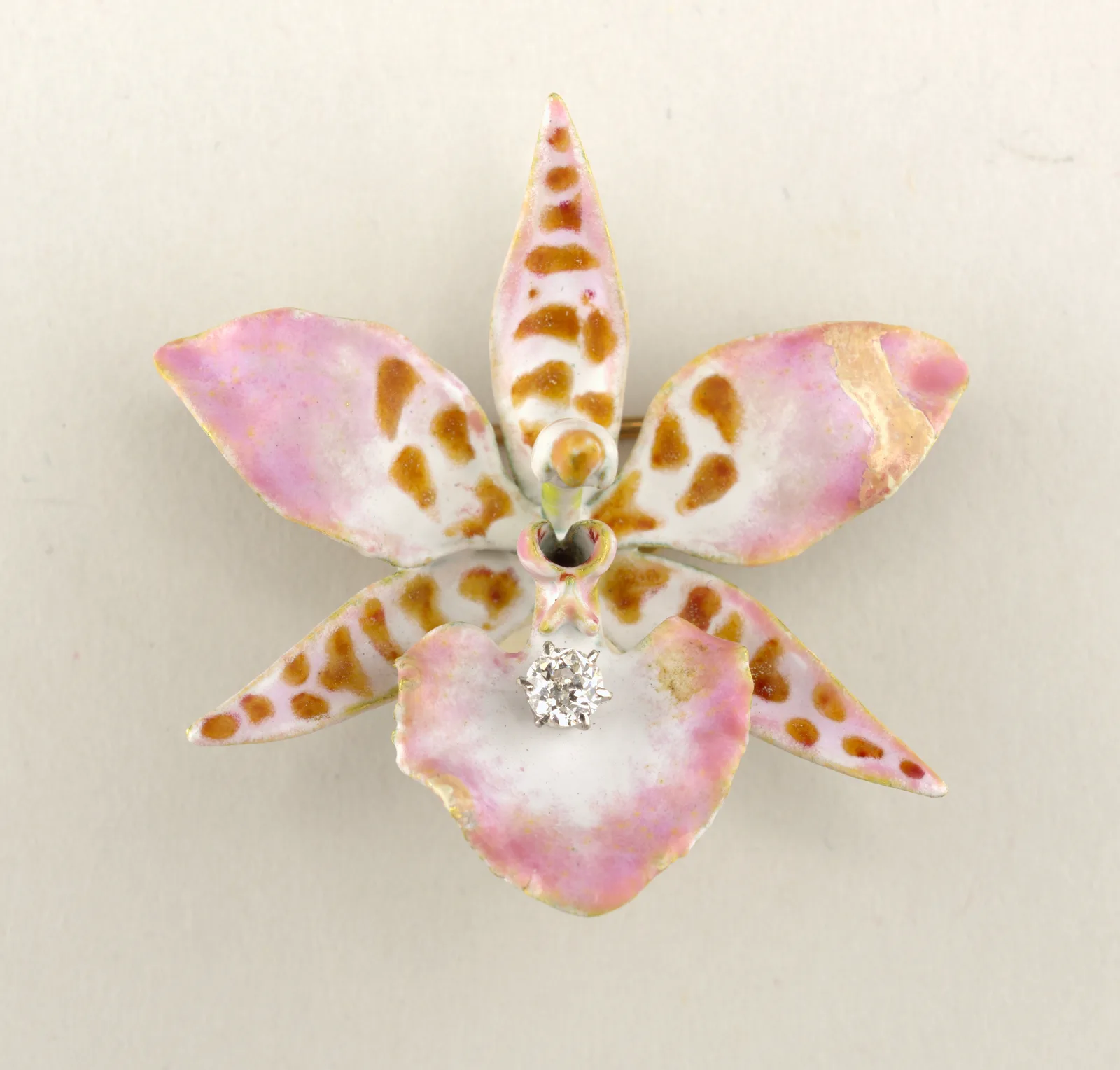 Enamel orchid brooch with cream and blush petals, dark spots, and a diamond set on the lower lip