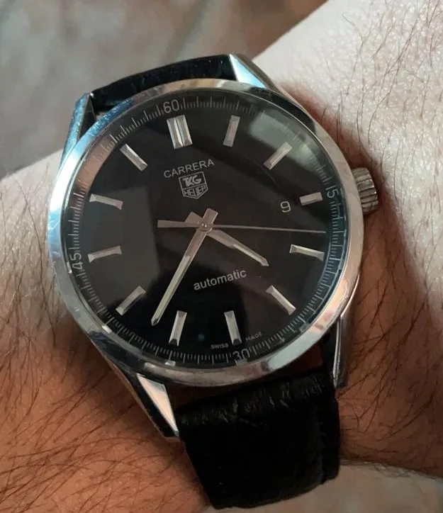 TAG Heuer Carrera Calibre 5 with a black dial, applied markers, and a tachymeter bezel, shown off the wrist on a white ground