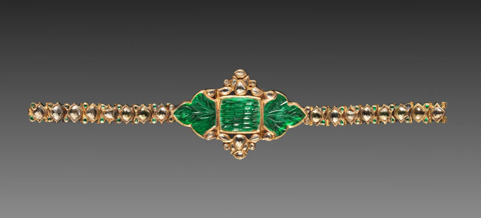 Mughal gold bracelet with a fluted emerald center and two bands of diamonds set in a continuous recessed gold line