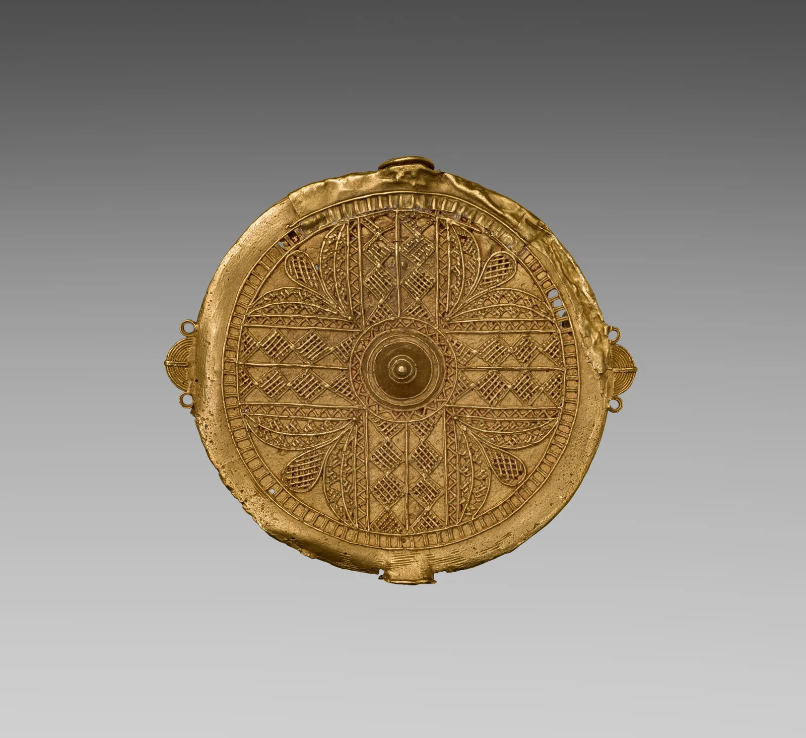 Asante gold disk pendant whose face is written as a radiating field of small lozenges and diamonds around a central boss