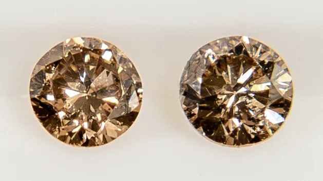 Two small round brilliant cognac diamonds side by side on a white ground