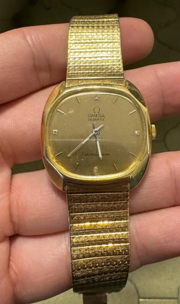 Omega Constellation in yellow gold with an integrated bracelet, day and date windows, and claws on the bezel, shown off the wrist on a white ground