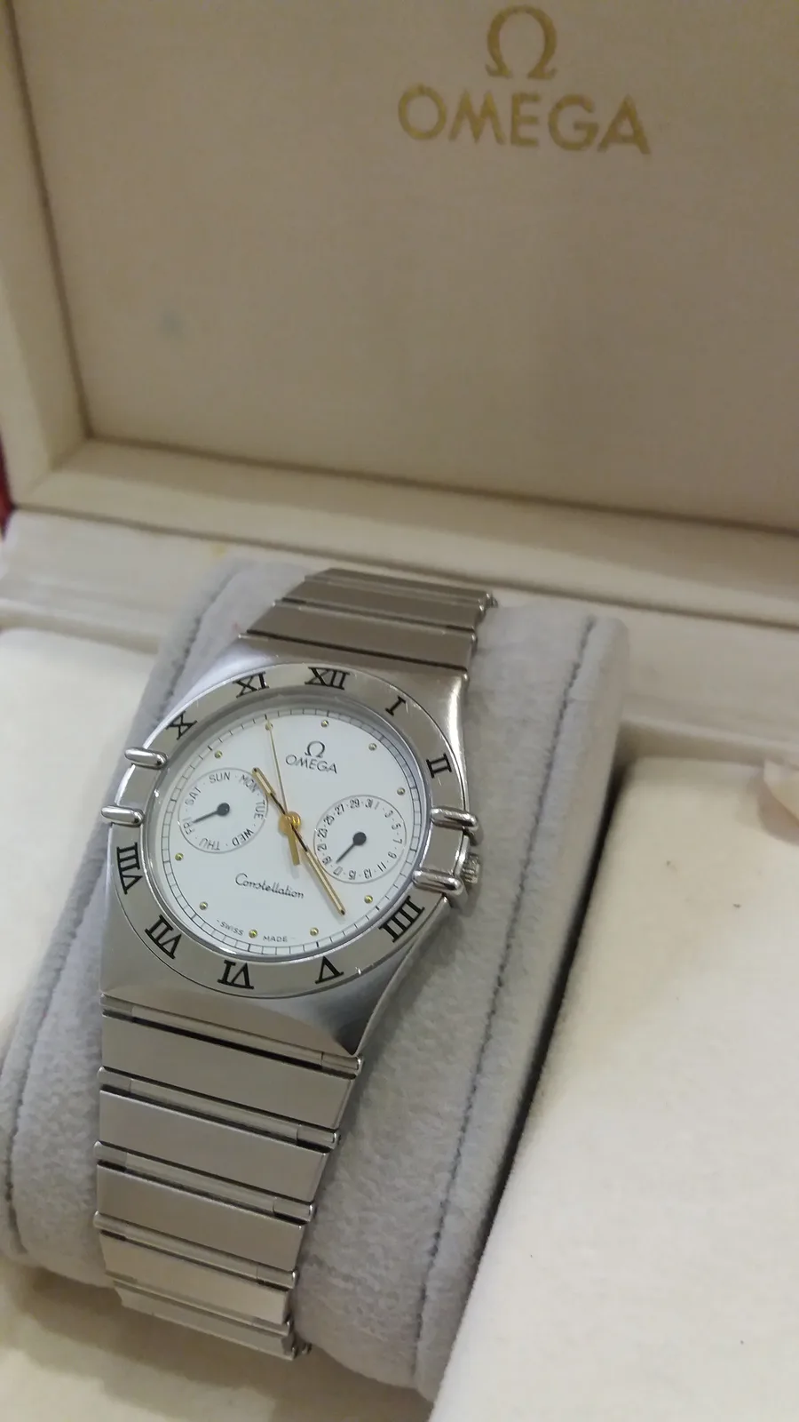 Omega Constellation Manhattan in two-tone metal, claws on the bezel and the caseback medallion visible, shown off the wrist on a white ground