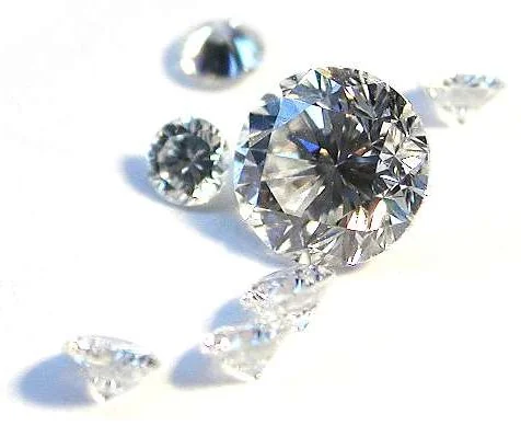 Loose brilliant-cut diamonds on a white surface, one seen in profile with the pavilion tapering to a point