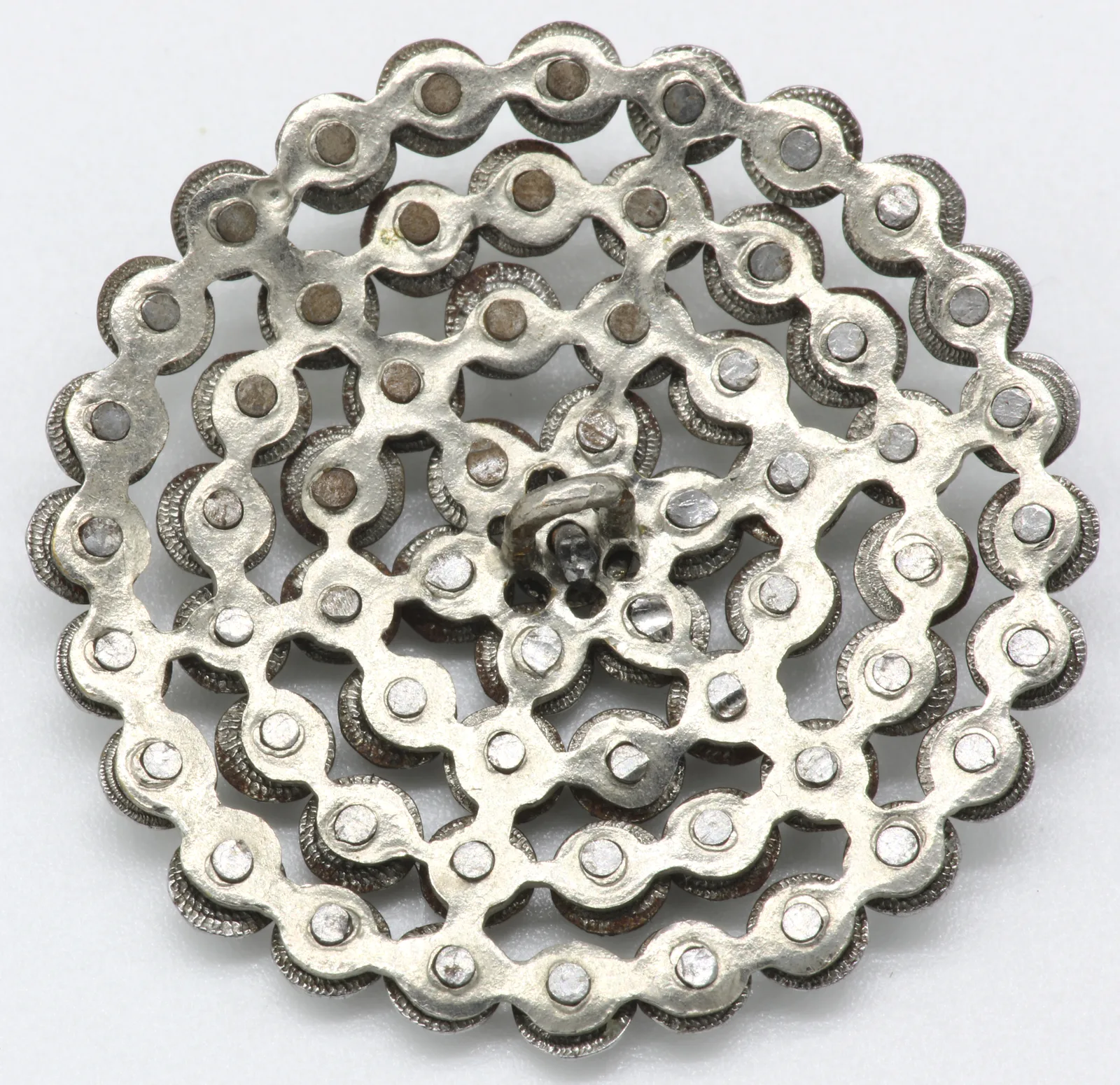 The back of a cut-steel button on a white ground, concentric rings of rivets around a central shank
