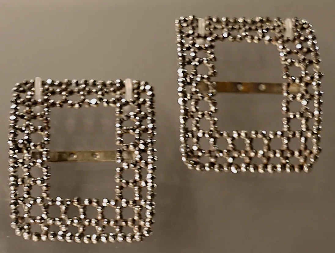 A pair of openwork cut-steel buckles with faceted studs and a bow at the top of each frame, on a white ground