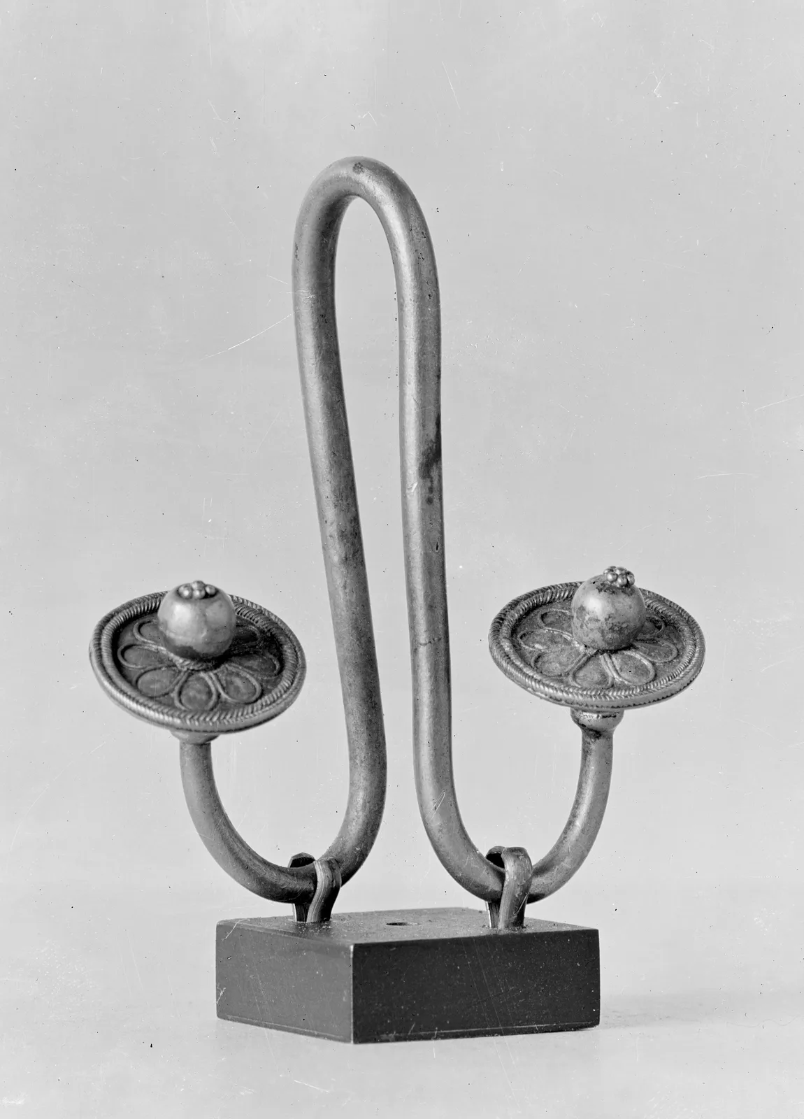 A Greek electrum earring in the form of a double hook, pale gold, with a small bead at the center