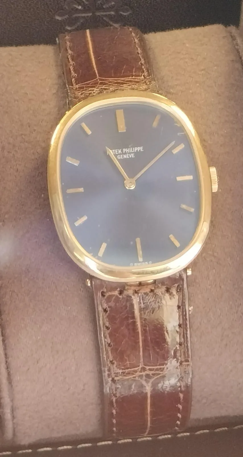 A gold Patek Philippe Golden Ellipse with a blue sunburst dial and an integrated gold bracelet, shown off the wrist on a white ground