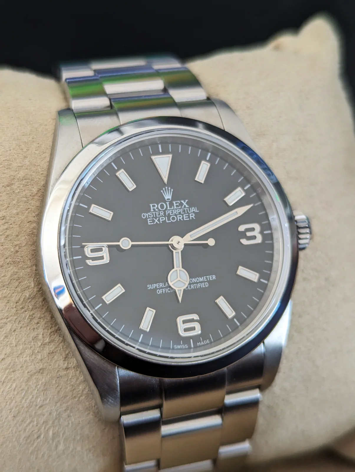 Rolex Explorer reference 114270 with a black dial and numerals at 3, 6, and 9, shown off the wrist on a dark ground