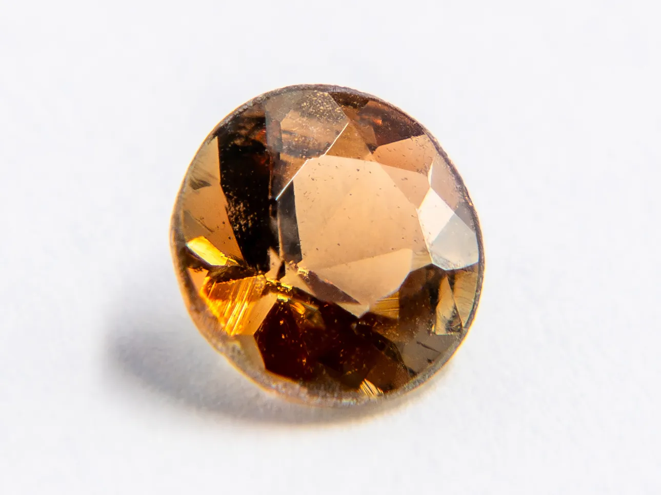 Round faceted andalusite on a white ground, flat faces in brown, olive, and rusty orange around a calm center