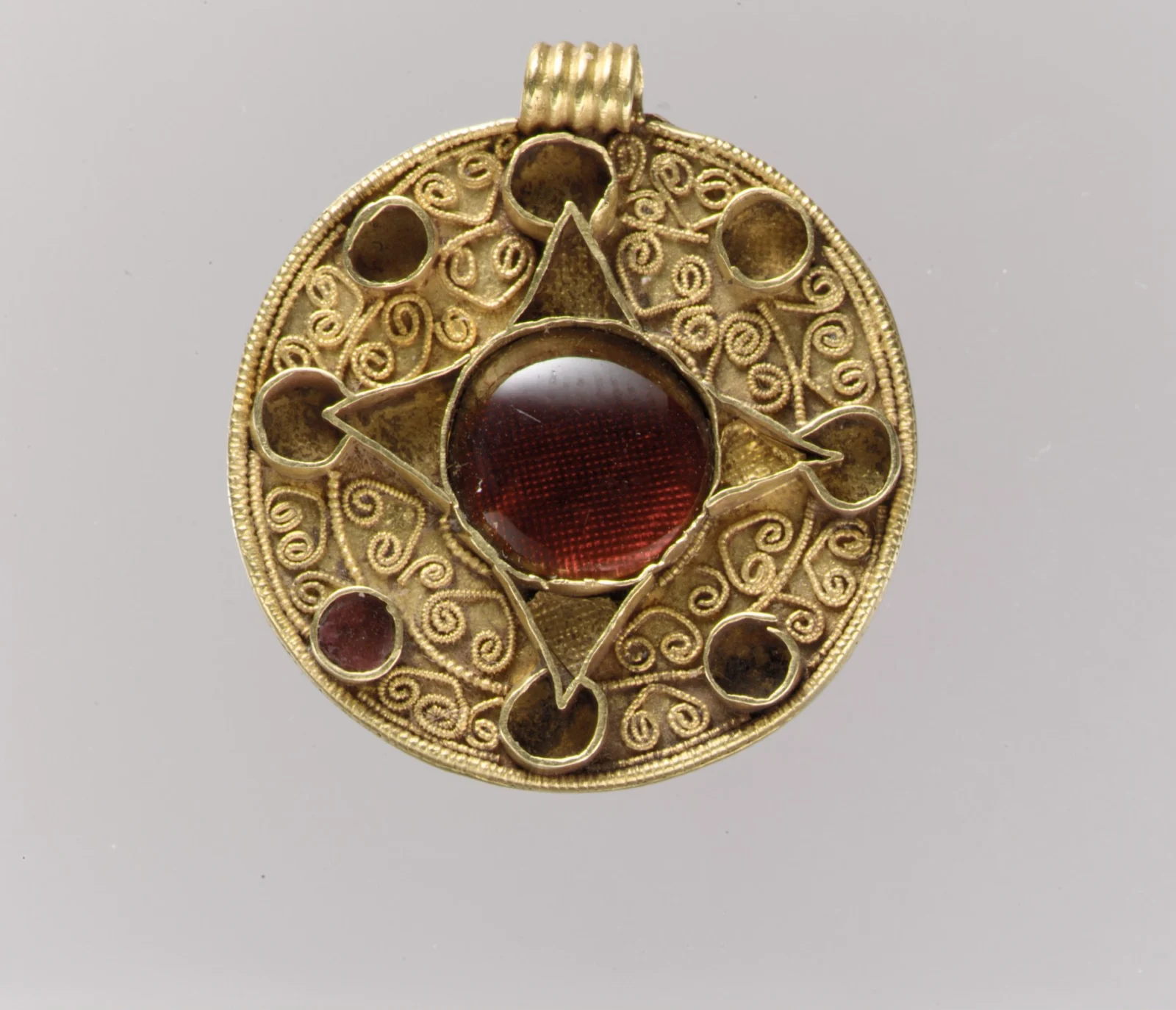 Anglo-Saxon gold pendant with a central cabochon garnet over patterned foil, a four-pointed star, and a ring of filigree