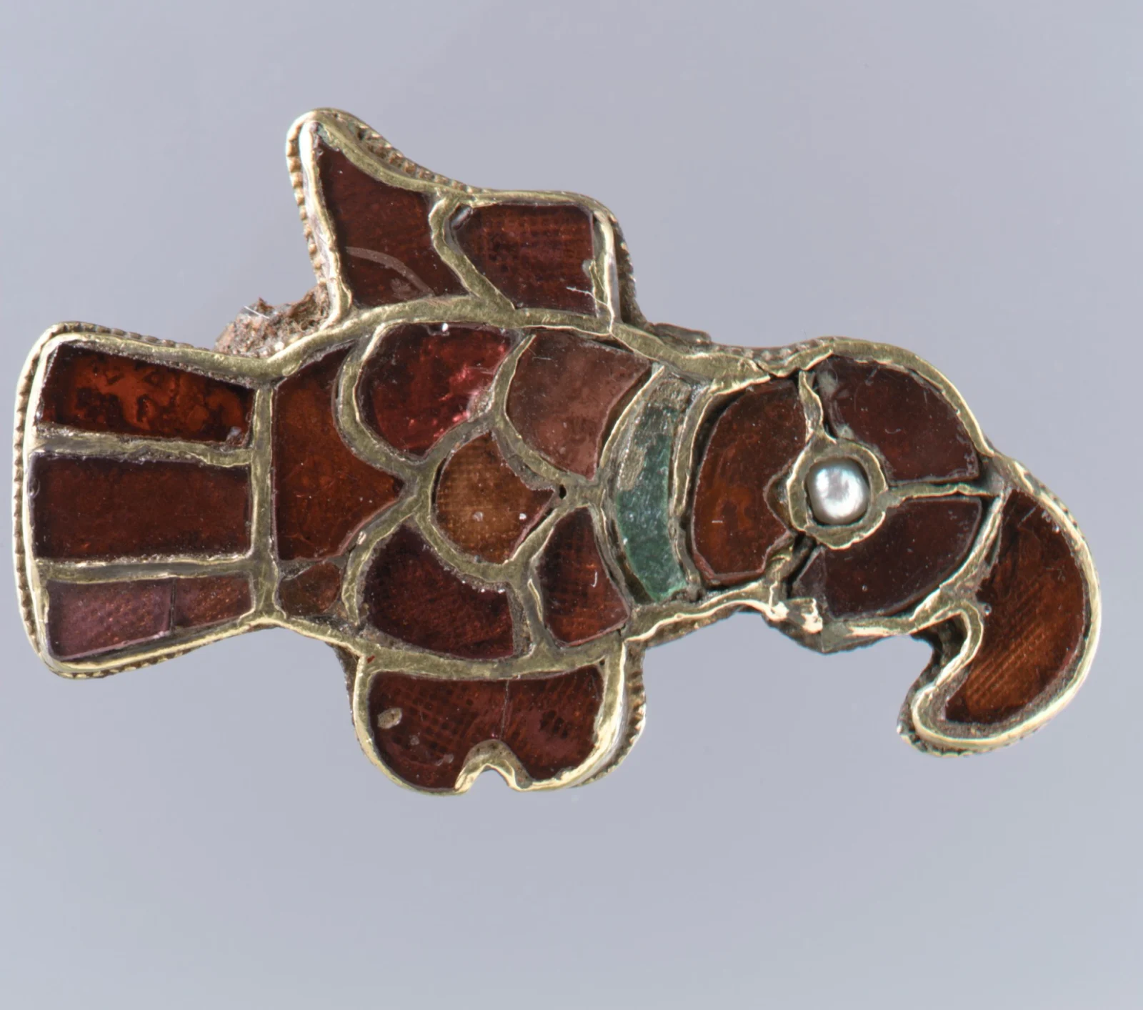 Frankish gold bird brooch in cloisonné garnet with patterned foil visible through the red cells and a pearl eye