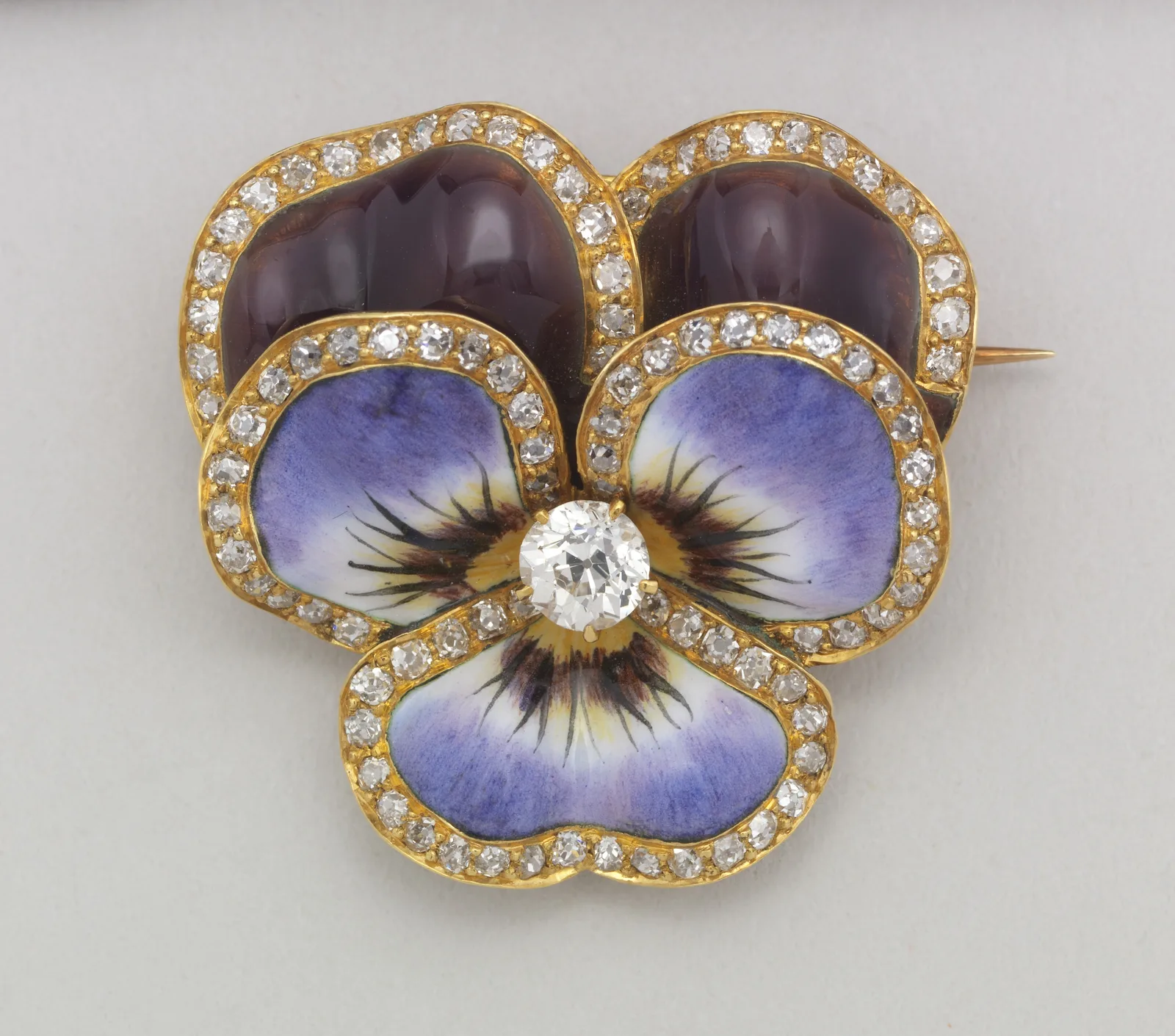 Enameled gold pansy brooch with two dark upper petals, three pale violet lower petals, a diamond center, and a diamond outline around each petal