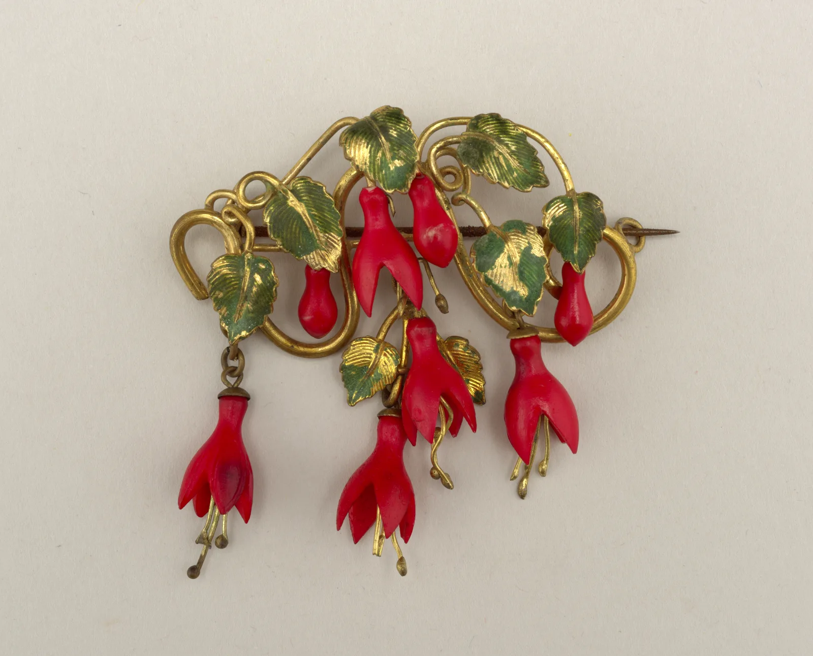 Gold brooch formed as a curled vine with green enamel leaves and hanging red fuchsia flowers and buds