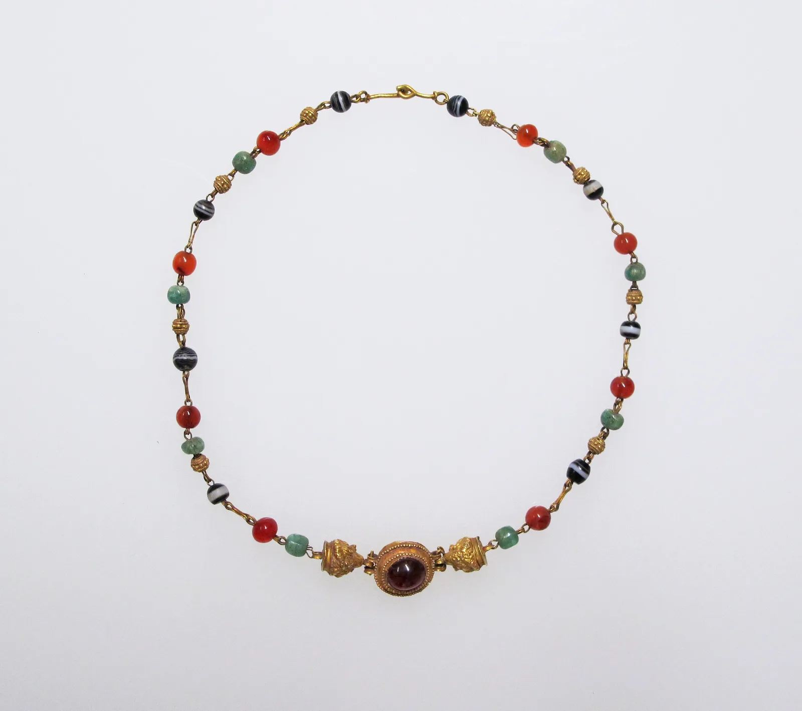 Roman gold necklace of emerald, carnelian, and banded-onyx beads with a large circular cabochon garnet at the center between lion-head terminals