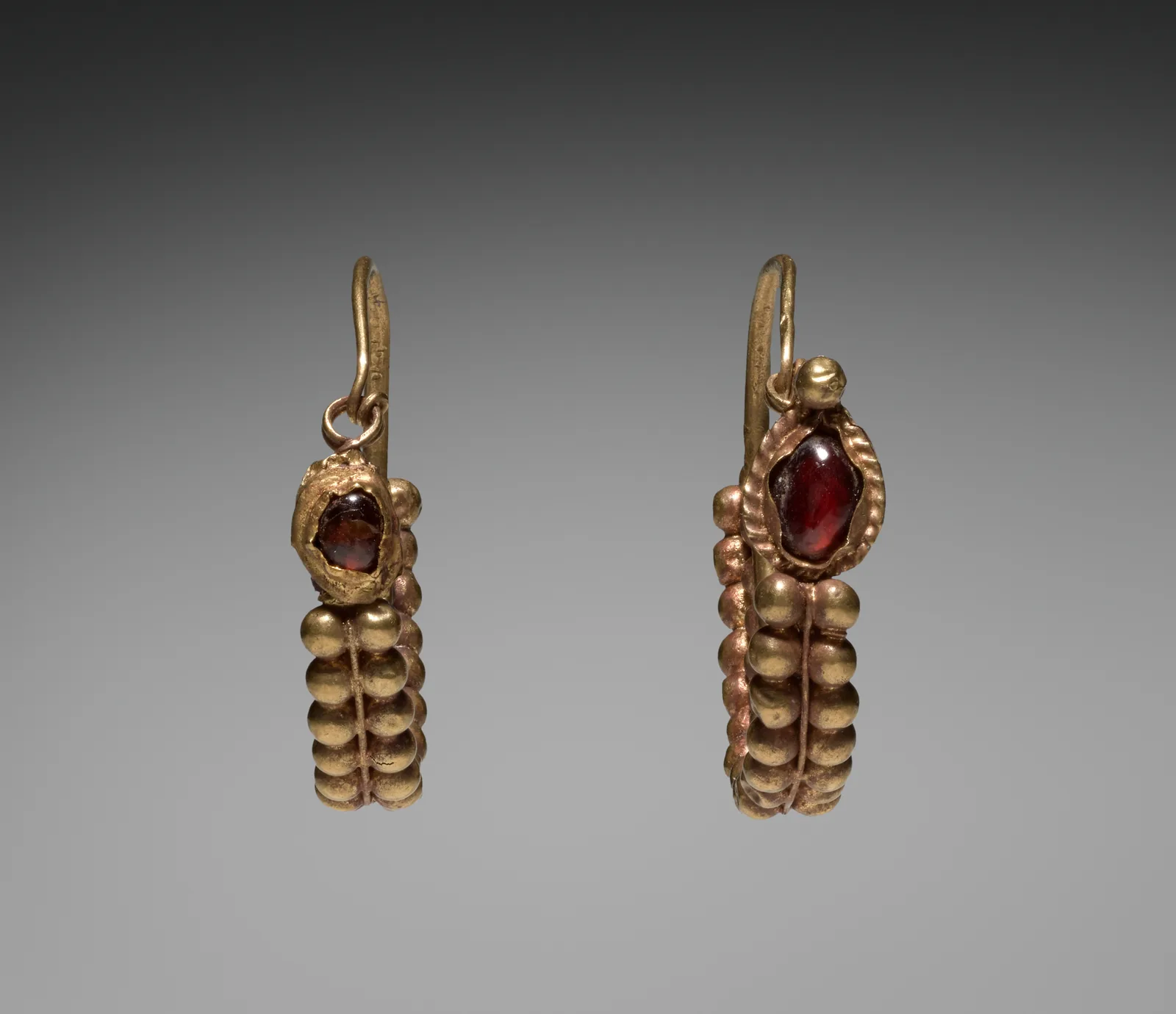 Pair of Roman gold earrings from Syria, each a vertical band of gold beads set with a deep oval cabochon garnet in a scalloped bezel