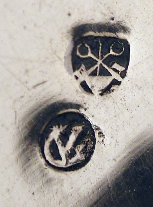 Close catalog still of two hallmarks punched into silver, a shield of crossed keys above a circular letter stamp