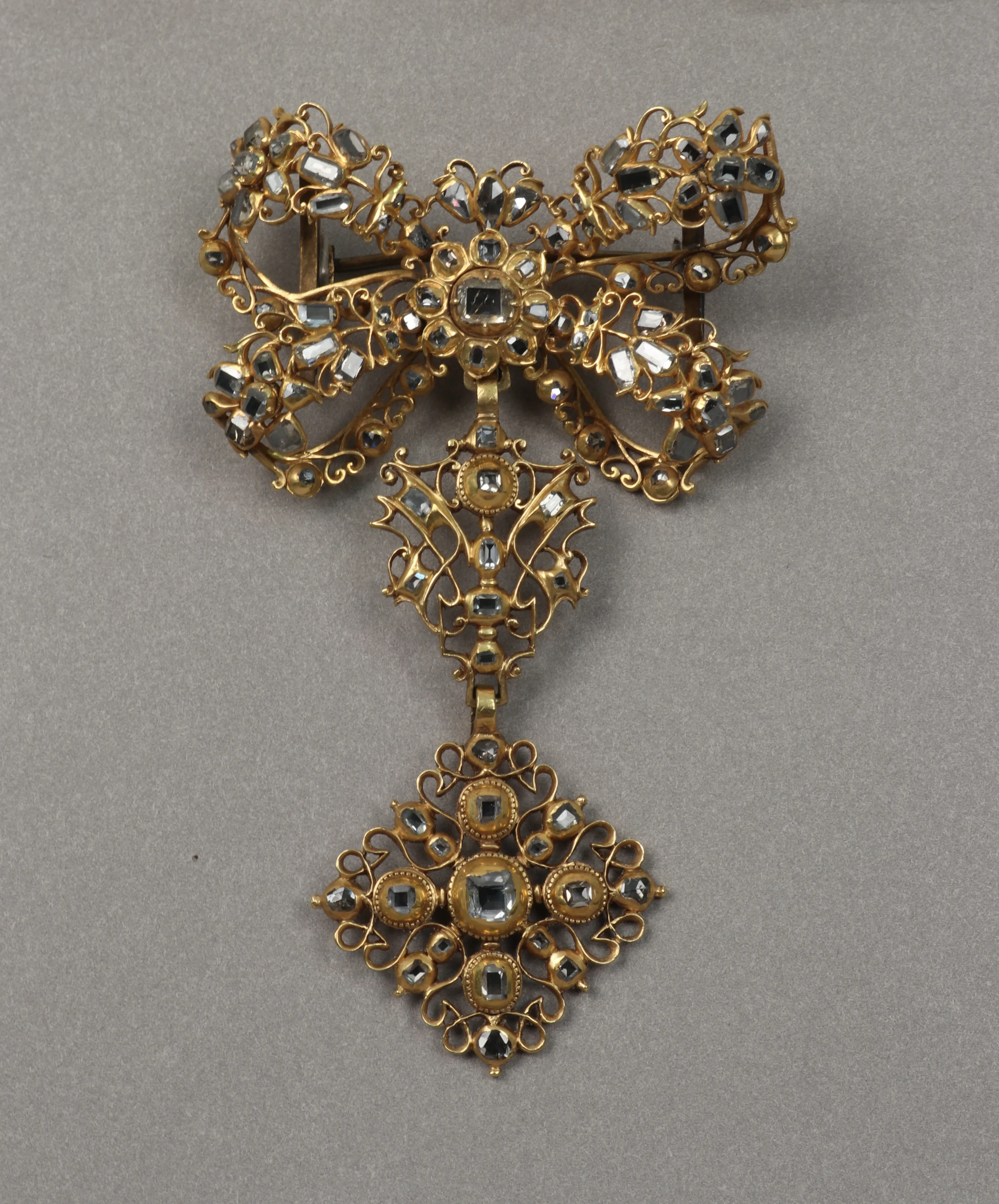 Eighteenth-century gold bow brooch with a small diamond halo at the knot and a diamond-shaped pendant whose center stone sits in another ring of light
