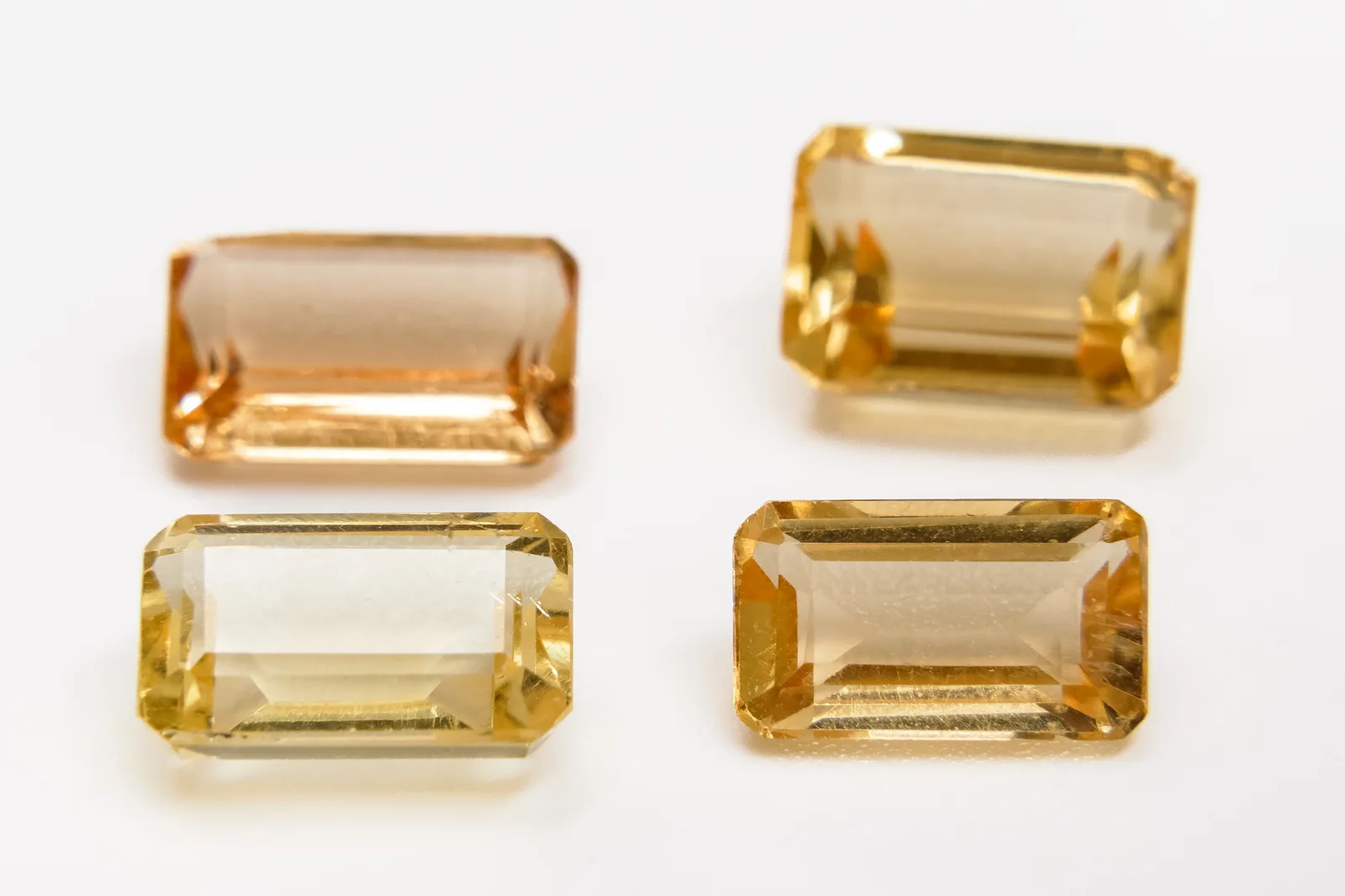 Four emerald-cut golden beryl gems in a row, yellow step-cut stones on a white ground