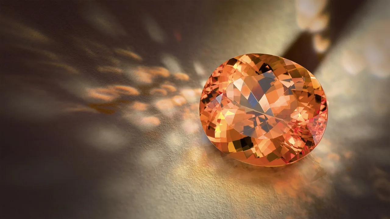 An oval faceted imperial topaz, golden to pink-orange, on a dark ground