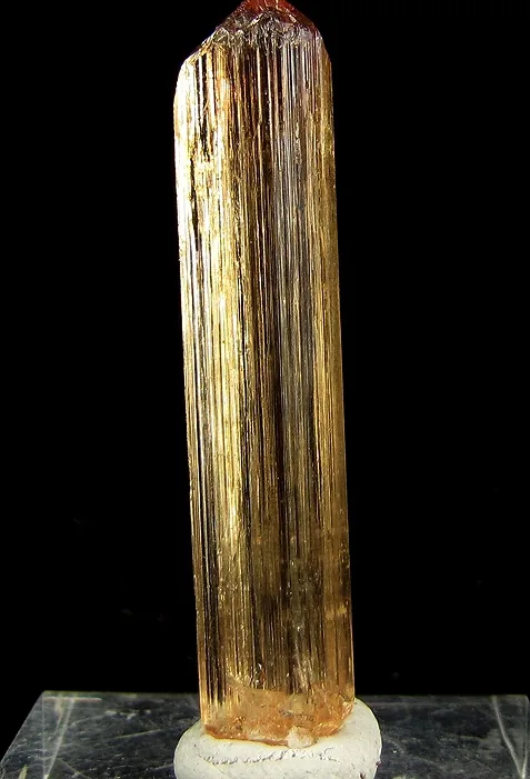 A long striated golden-orange imperial topaz crystal from Ouro Preto on a white ground