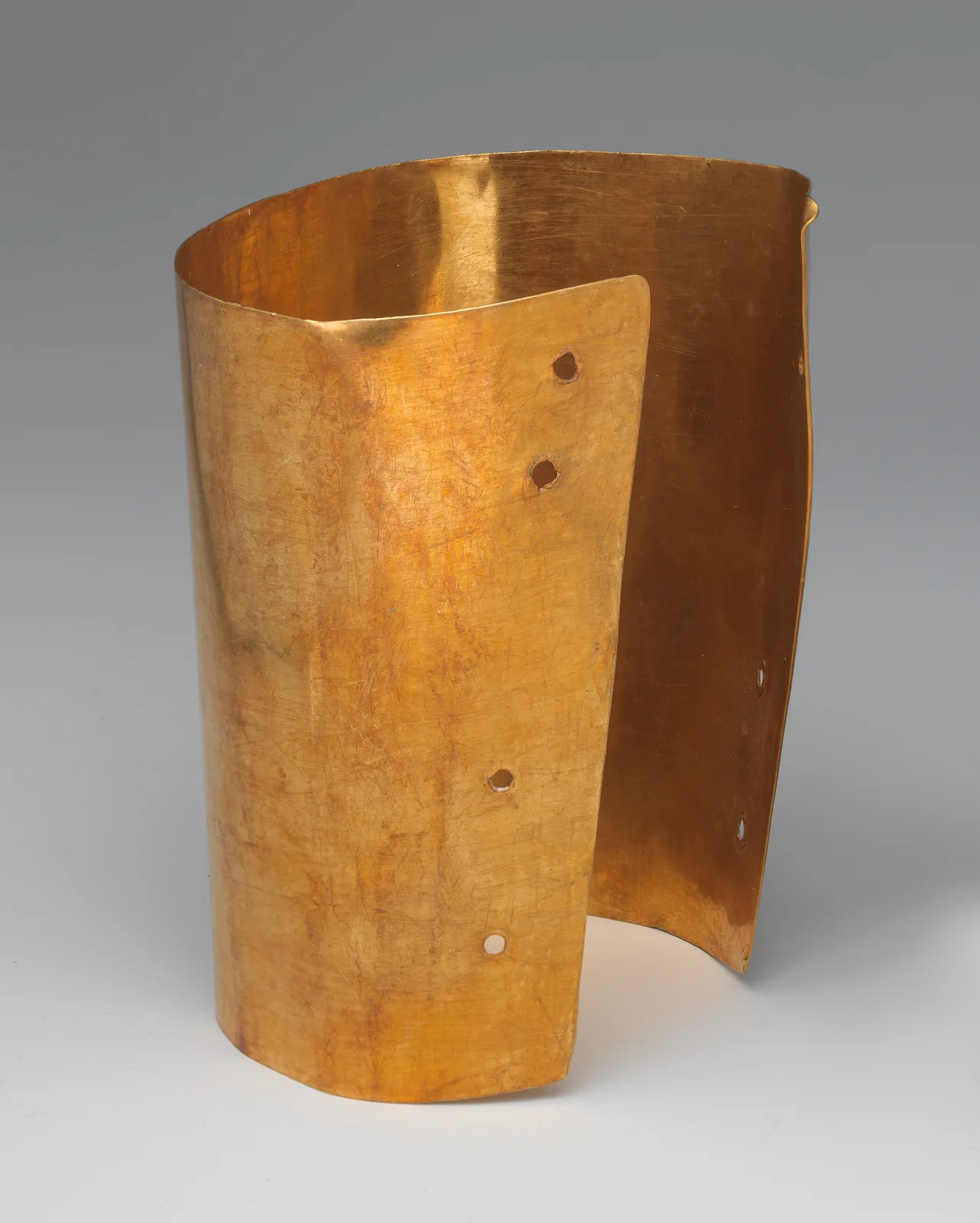 Pre-Columbian gold cuff standing as an open cylinder with punched holes along the vertical edge