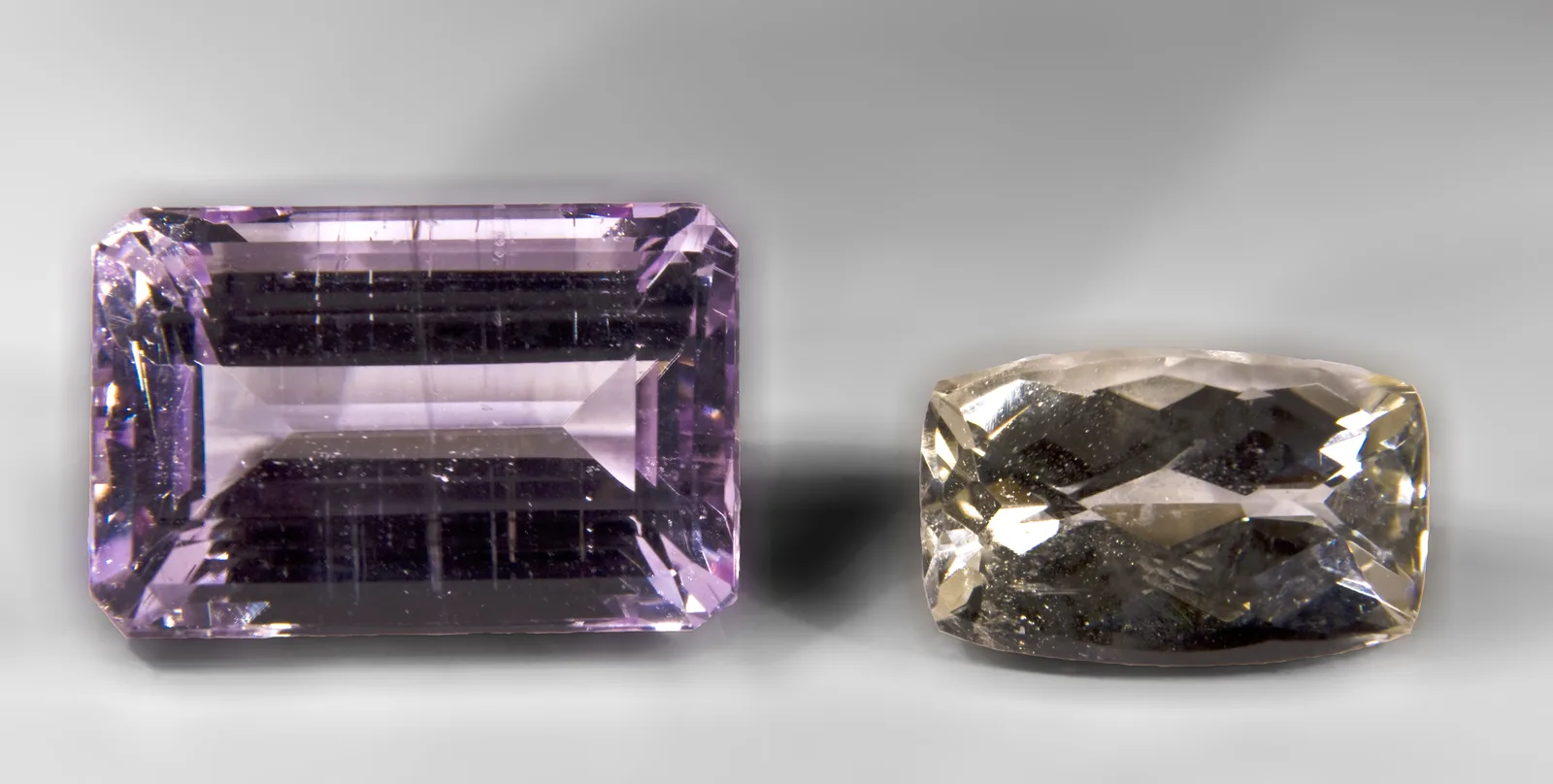 Two faceted spodumene gems on a white ground, a lilac-pink kunzite beside a green hiddenite