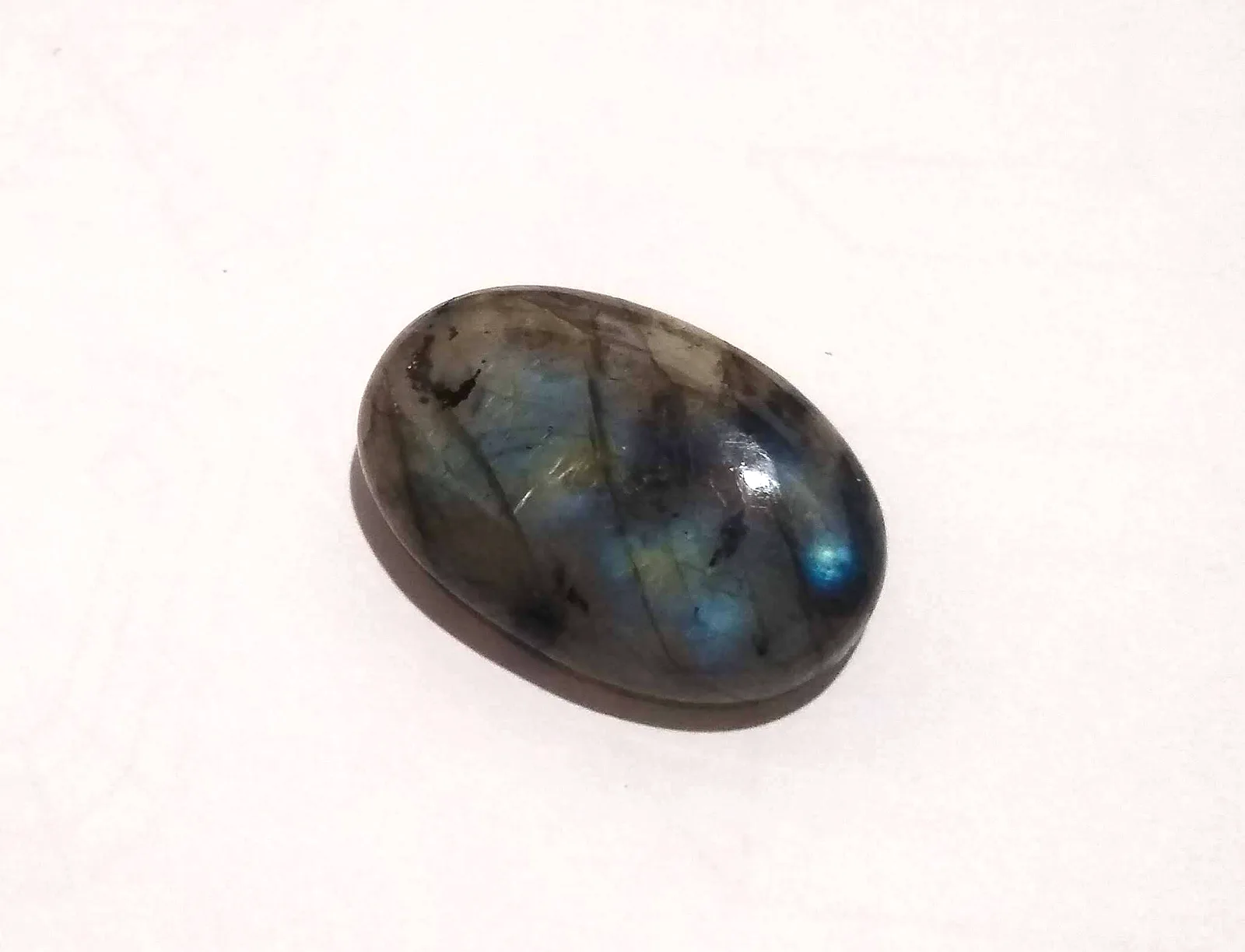 Polished Brazilian labradorite cabochon on a light ground, a cool flash crossing the dome