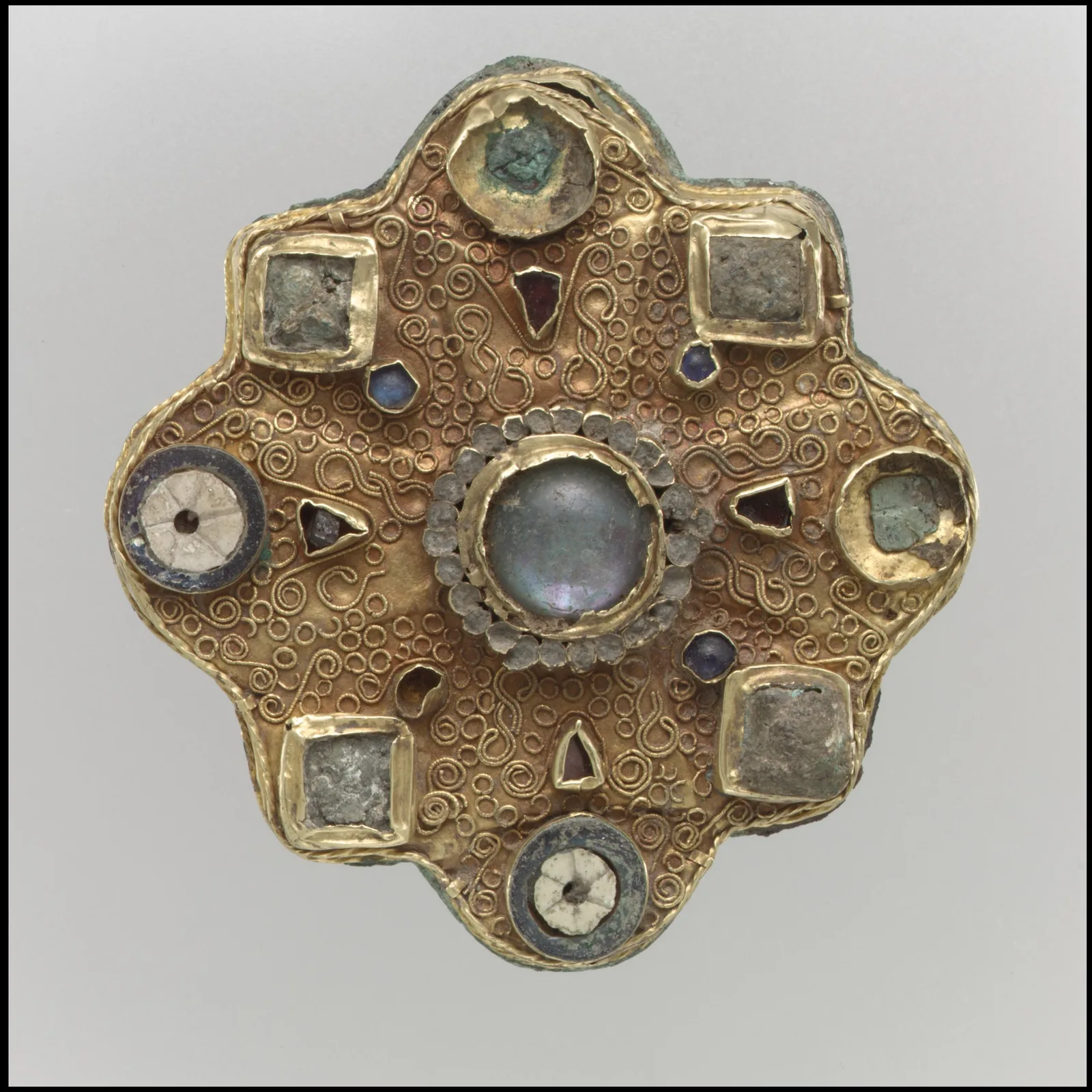 Frankish gold disk brooch with a large milky moonstone cabochon at the center, square glass settings, garnets, and a field of gold filigree