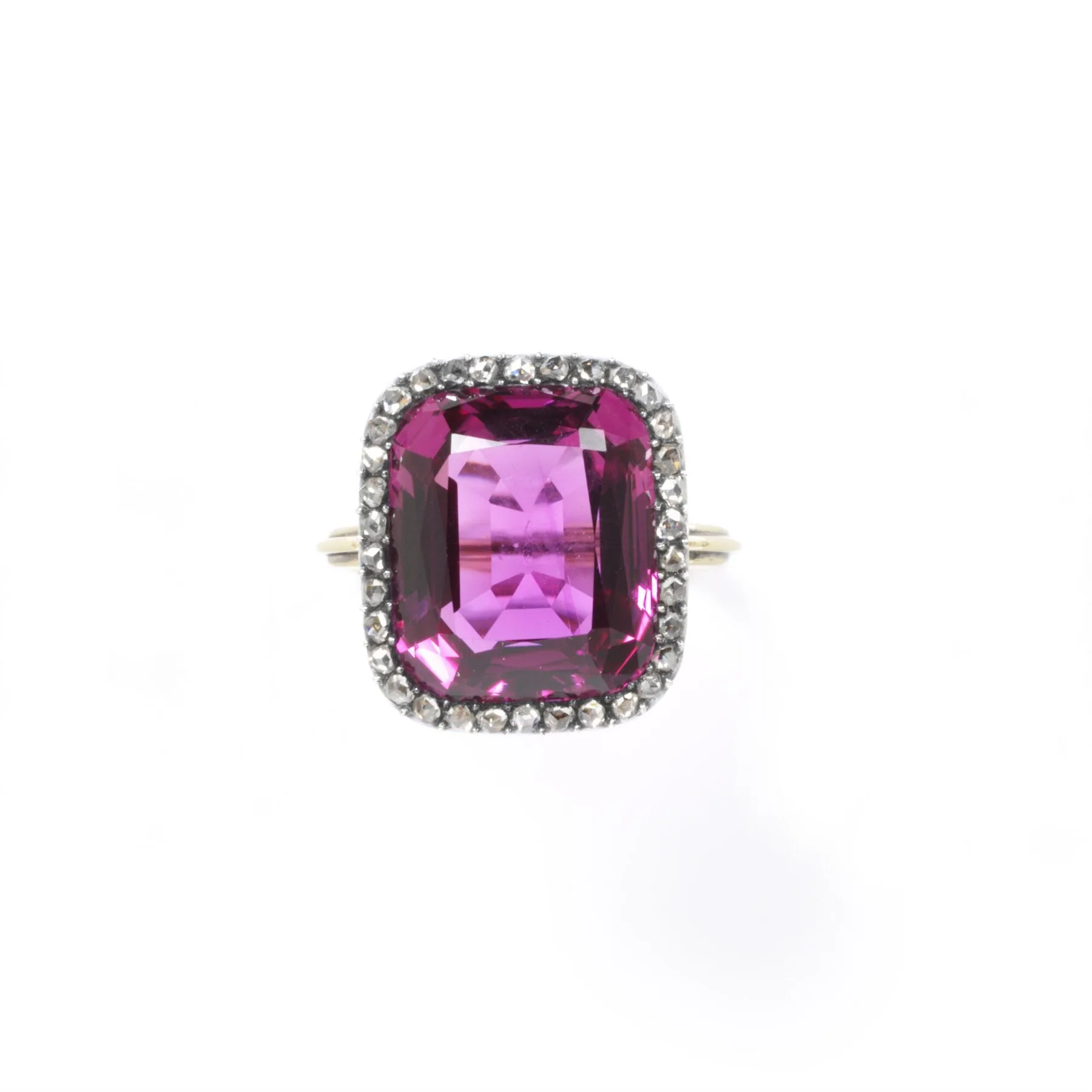 A deep rose-pink faceted oblong stone bordered by a diamond halo in a slim gold ring, already a soft pink transparent pane