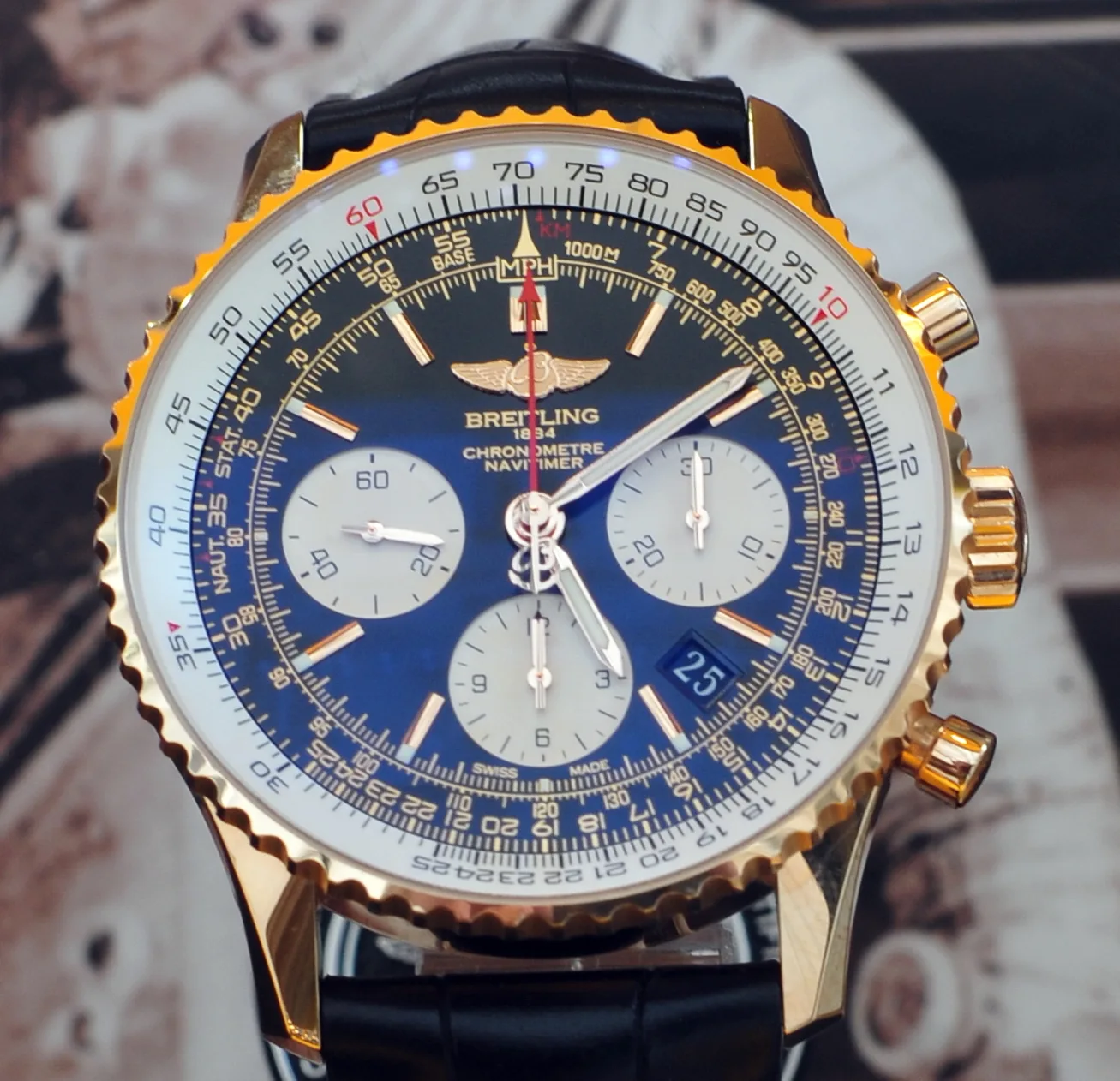 Breitling Navitimer chronograph with a gold case and black dial, shown off the wrist on a pale ground