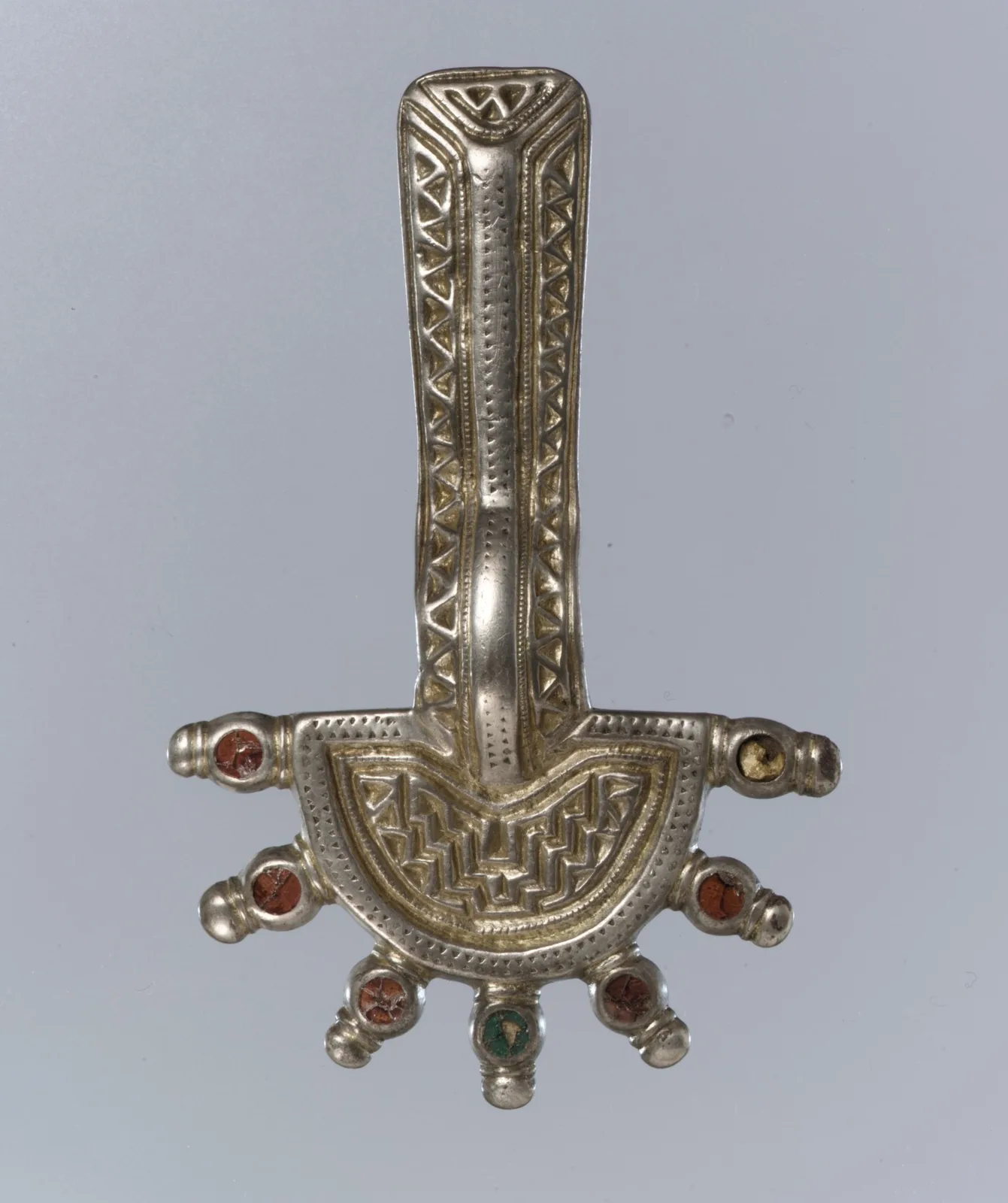 A Frankish silver-gilt bow brooch with black niello lines in geometric borders, garnets, and a round headplate