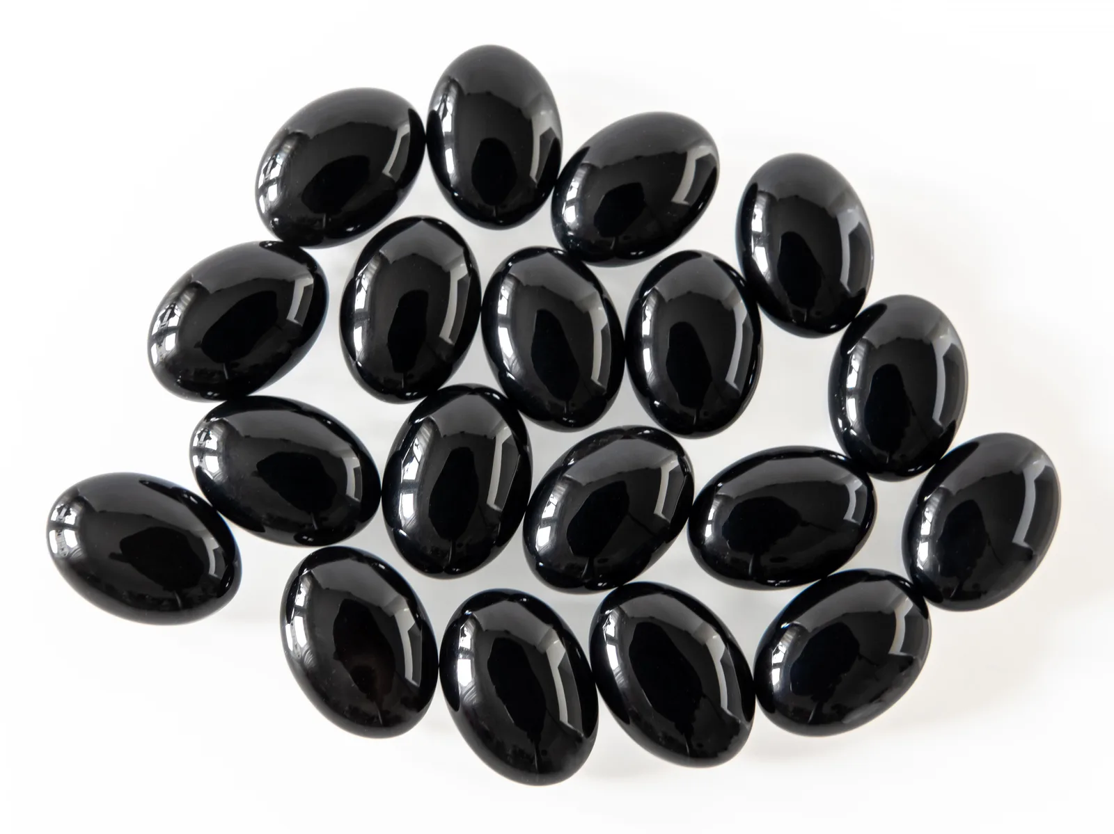 Studio still of polished black oval onyx cabochons arranged on a light ground