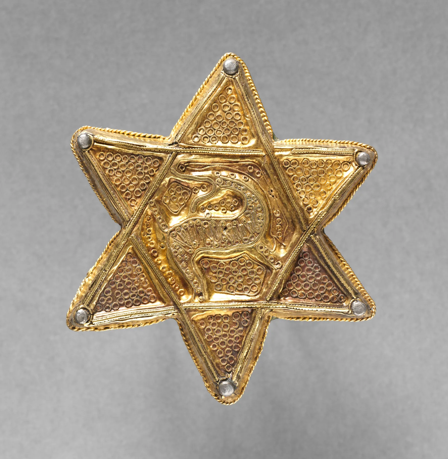 Early medieval gold six-pointed star brooch with twisted-wire borders and a curled animal in the center