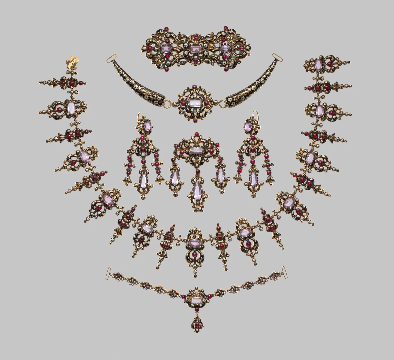 A Swiss gold, enamel, and paste parure of about 1840, with necklace, earrings, brooch, and bracelet laid on a white ground