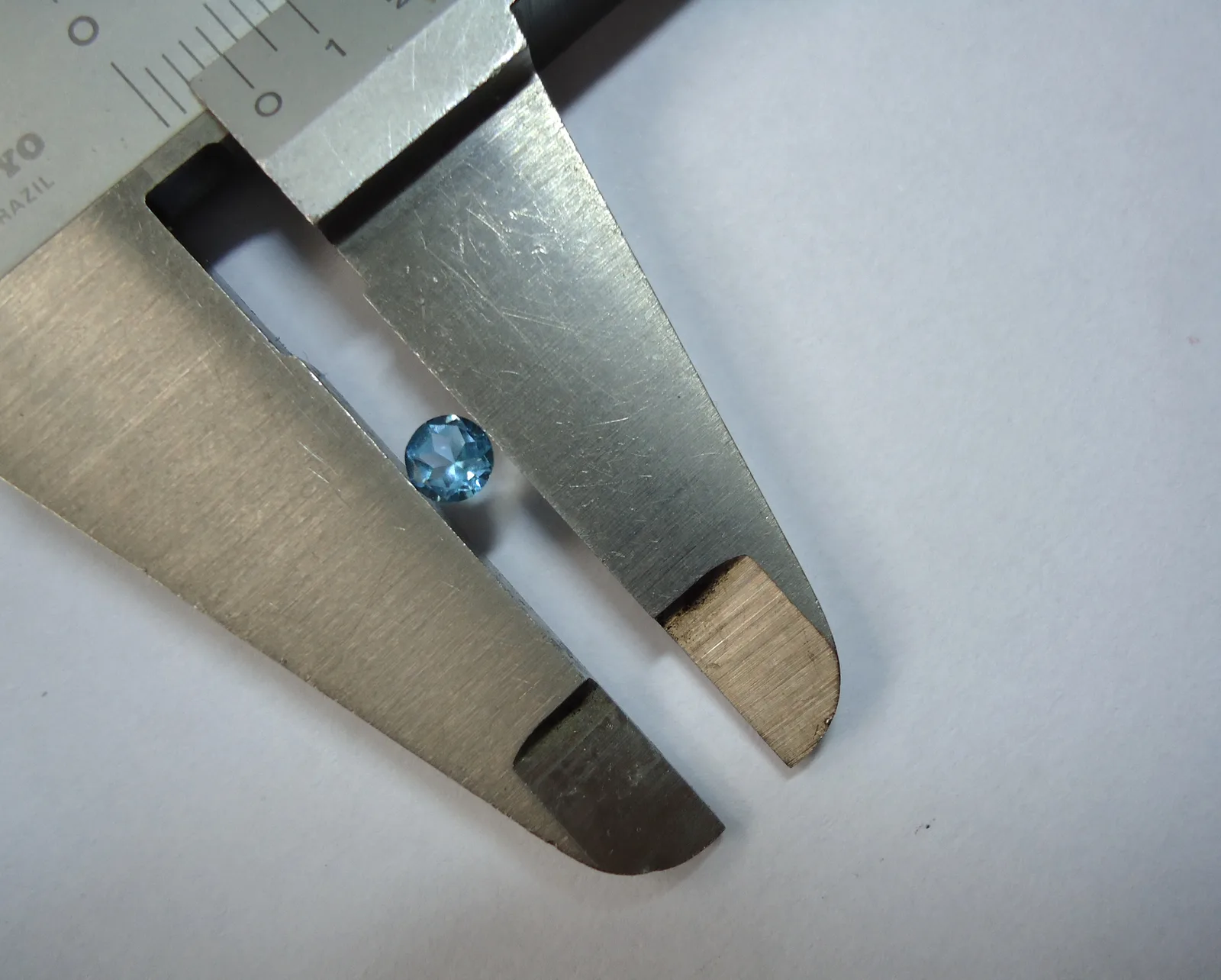 Blue topaz brilliant seen from the side in a jeweler’s measure, the pavilion the longer cone below the girdle
