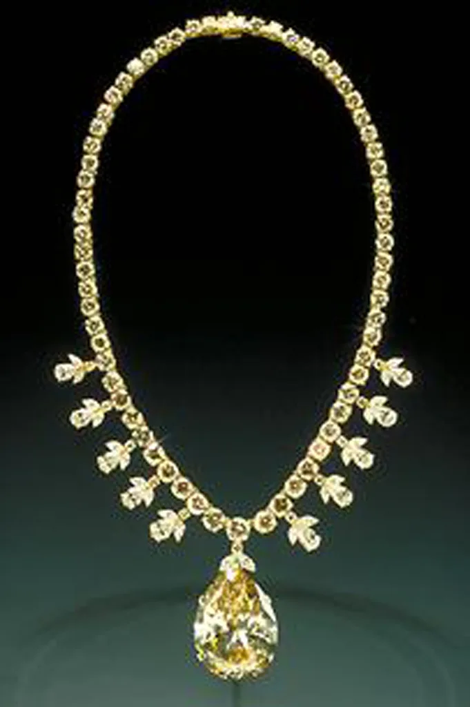 Large champagne pear-shaped diamond hung at the center of a yellow-gold diamond necklace in a museum case