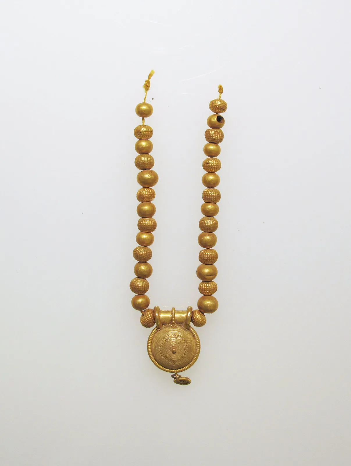 Etruscan gold necklace of smooth and textured spherical gold beads descending to a circular granulated bulla pendant