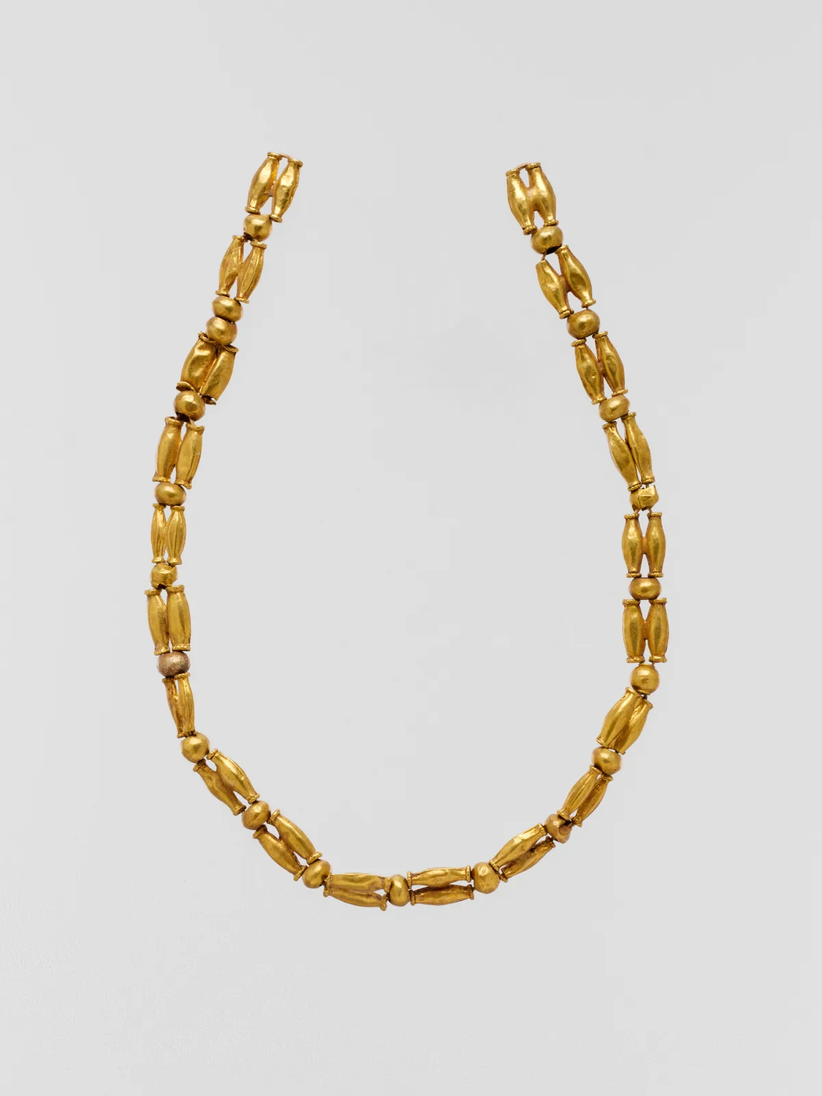 Cypriot gold necklace laid as a U of spherical spacer beads alternating with pairs of fluted elongated gold beads