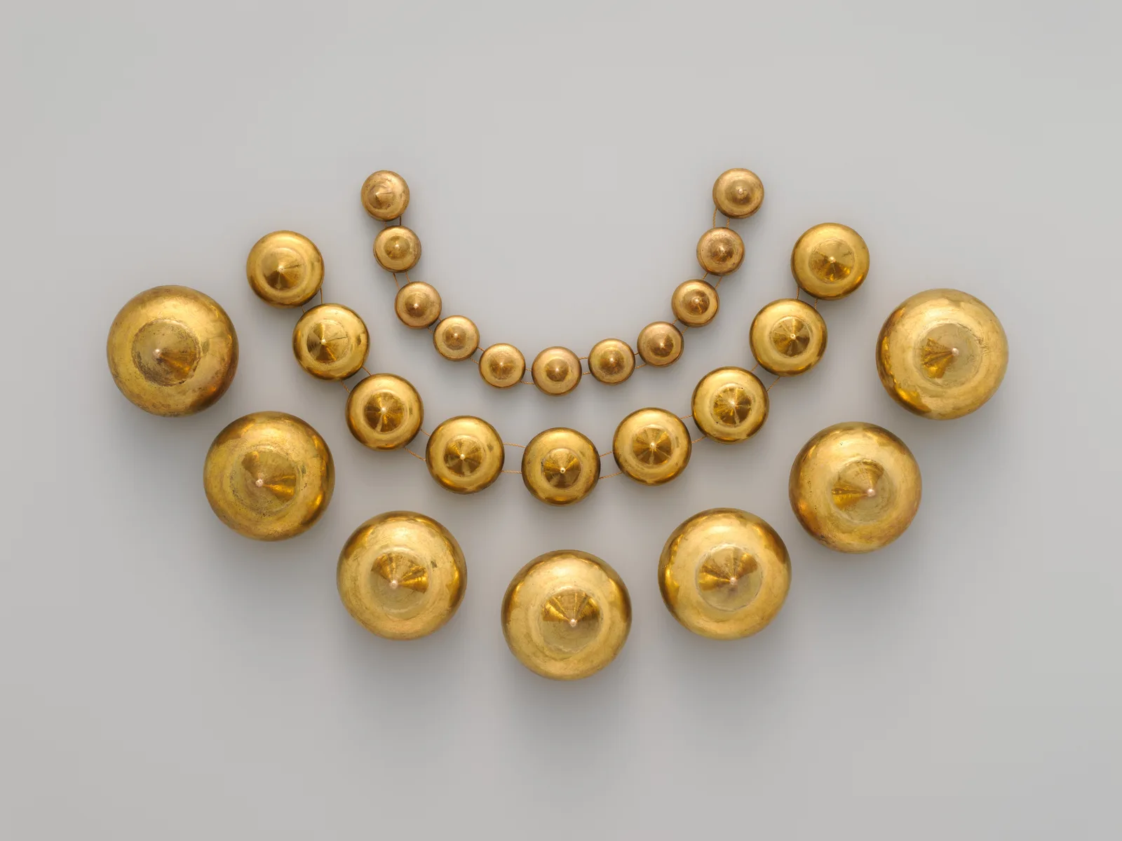 Moche gold necklace beads arranged in three concentric arcs, each a hemispherical gold dome rising to a small conical point