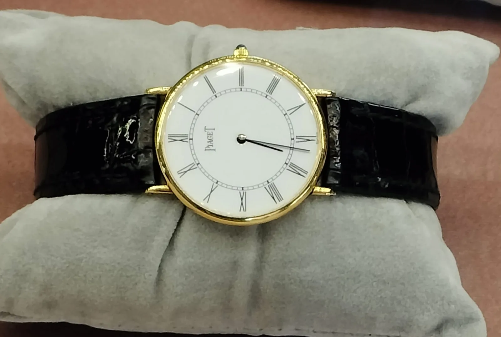 Yellow-gold Piaget Altiplano with a white Roman dial and a black leather strap on a gray cushion