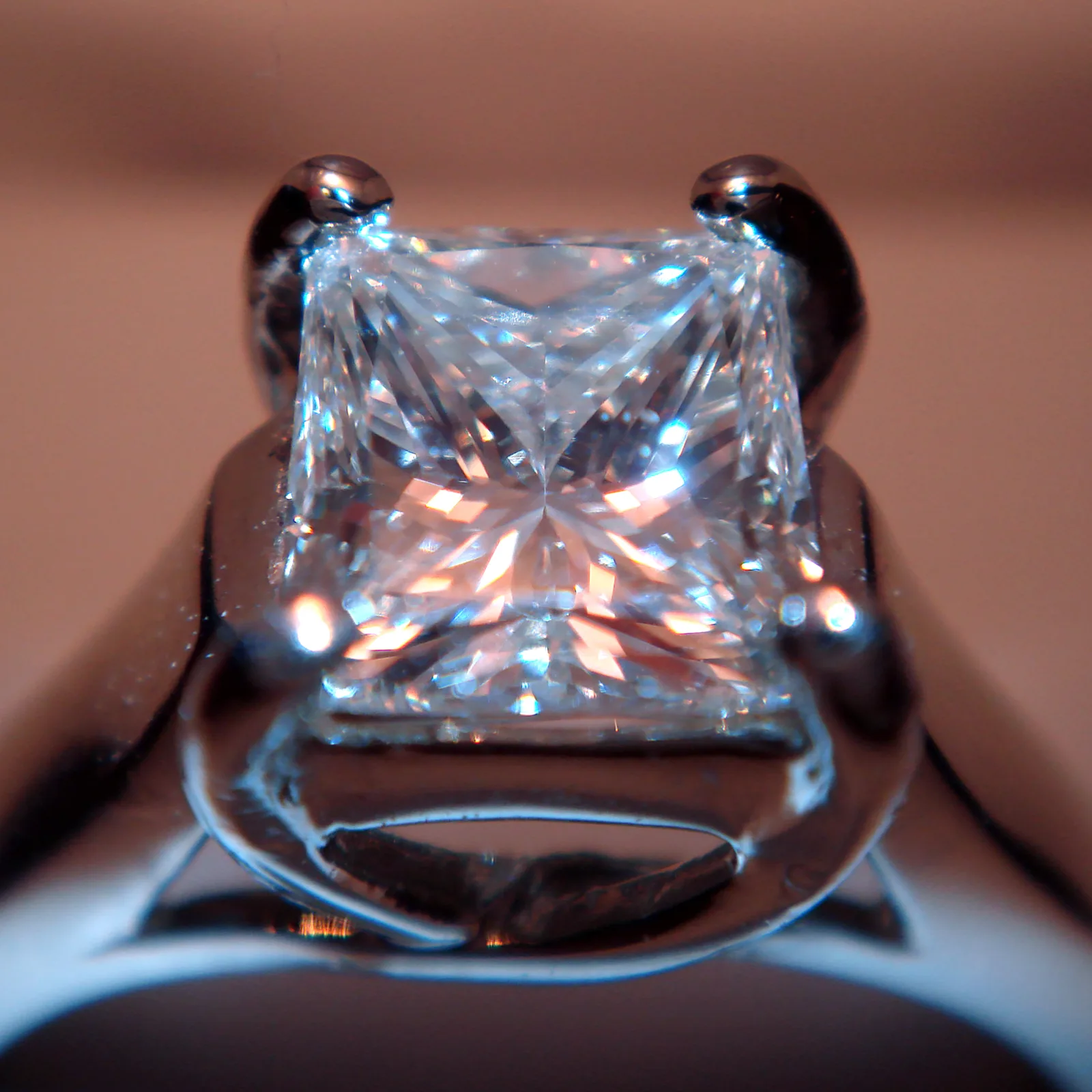 A princess-cut diamond face-up in a four-prong ring, sharp corners and an X of sparkle