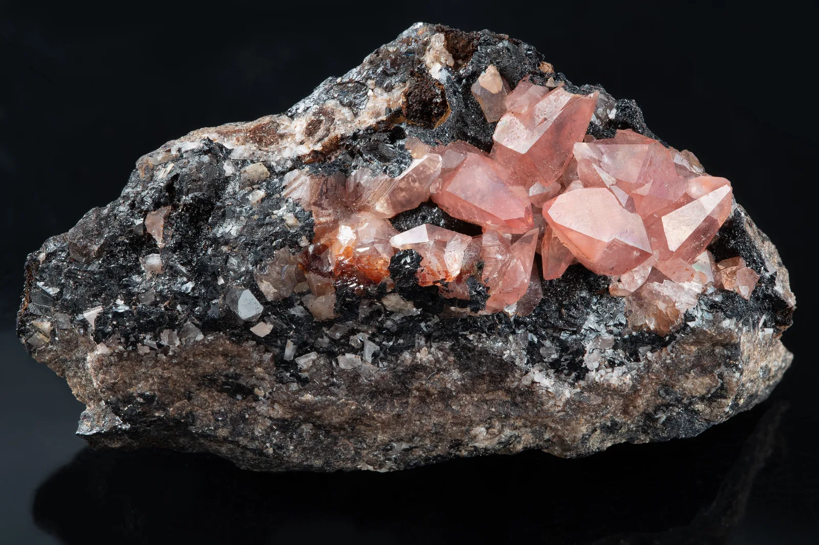 Bright pink-red rhodochrosite crystals with pointed faces on a dark matrix, a small Peruvian group on a white ground